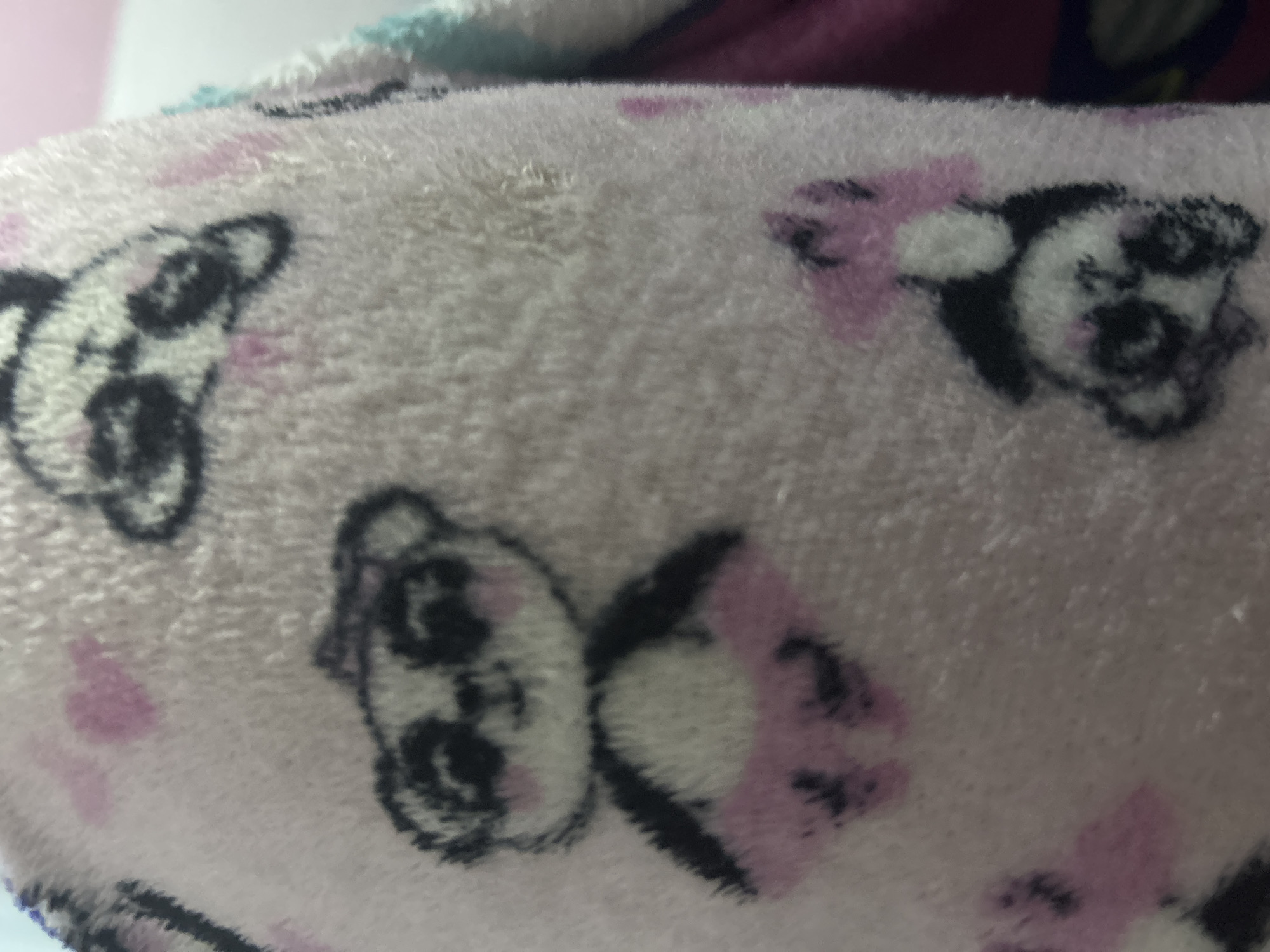 The image shows a close-up of a pink fuzzy fabric with a pattern of panda faces and pink bows. The pandas are primarily white with black markings around their eyes and ears. The pink bows are next to the pandas' heads. The fabric appears soft and plush. There is no information about the location, San Juan de Los Morros, Venezuela.
