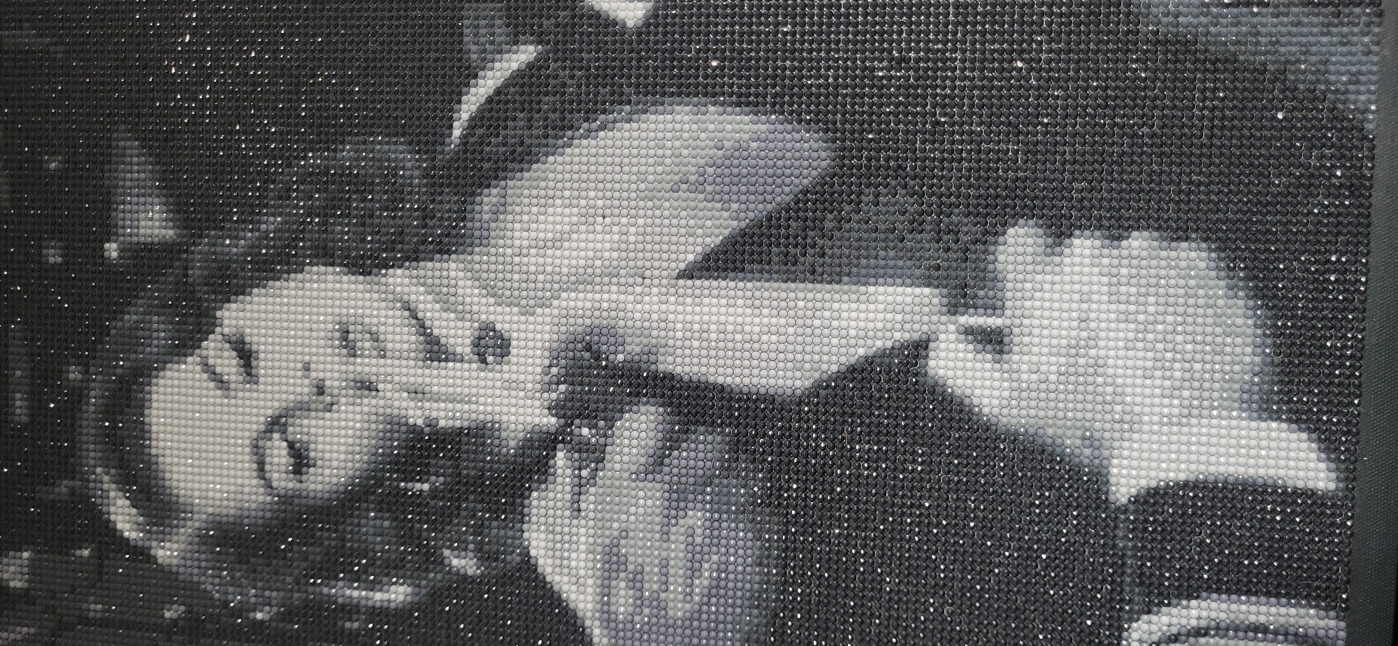 A black and white image comprised of small, shiny circular elements arranged to form a depiction of a person smoking. The person is seen from the shoulders up, lying down with their head to the left and the cigarette held in their right hand. The background is dark and blurred, suggesting a nighttime setting, although there are no clearly identifiable landmarks to place it in Moscow or any other specific location. The image is constructed to resemble a mosaic.