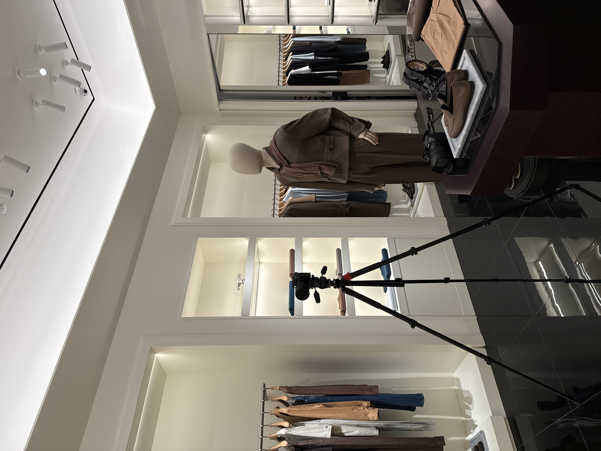 The image shows the interior of a retail store, likely a clothing boutique, with a mannequin dressed in a brown suit. The store has white walls and tiled floors, and clothing racks are visible on the walls. A camera on a tripod is visible. The location is the city of Perm, Russia.