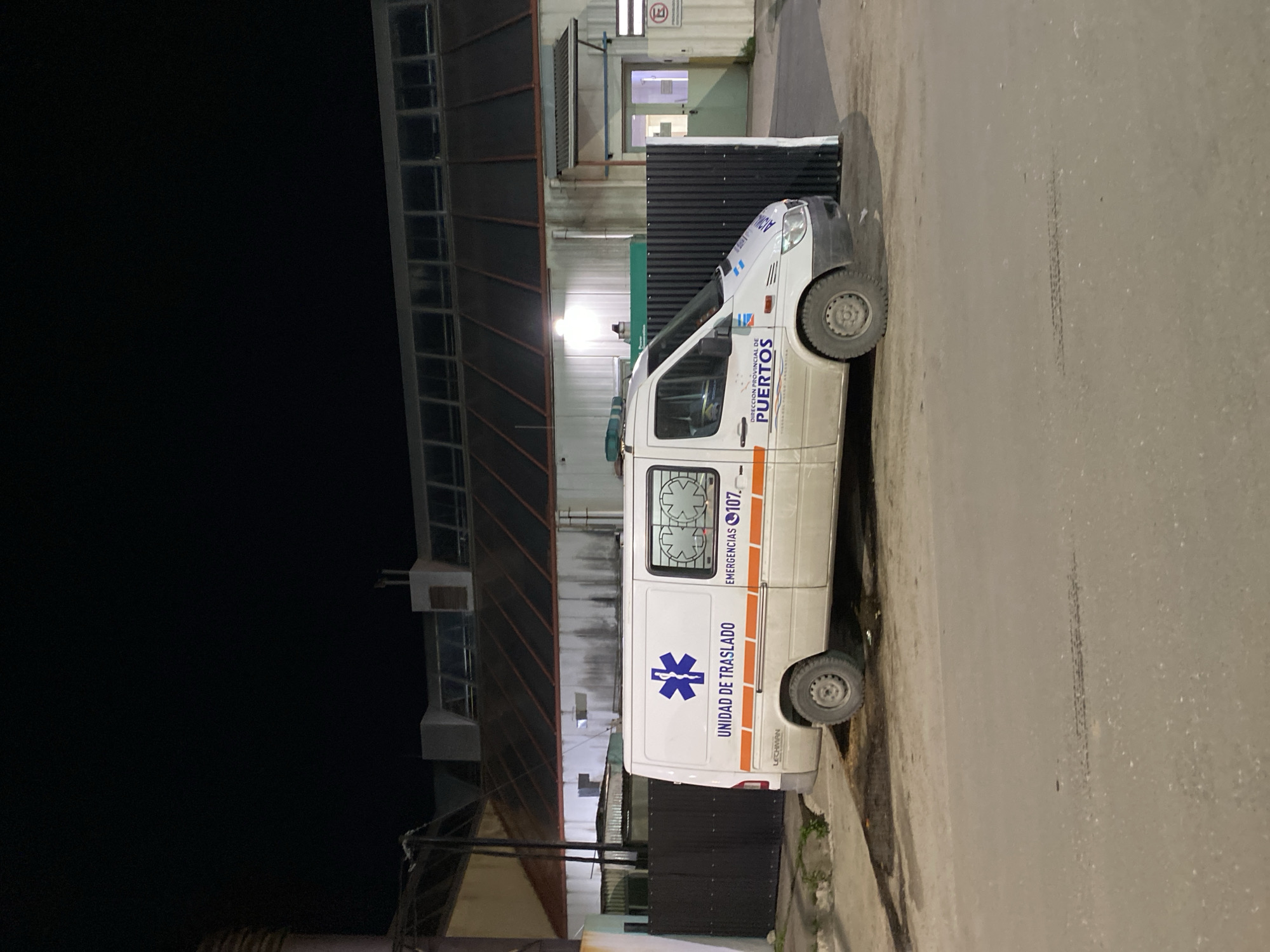 A white "Unidad de Traslado" ambulance is parked at the port in Ushuaia, Argentina. The vehicle has "Direccion Provincial de Puertos" written on it.
