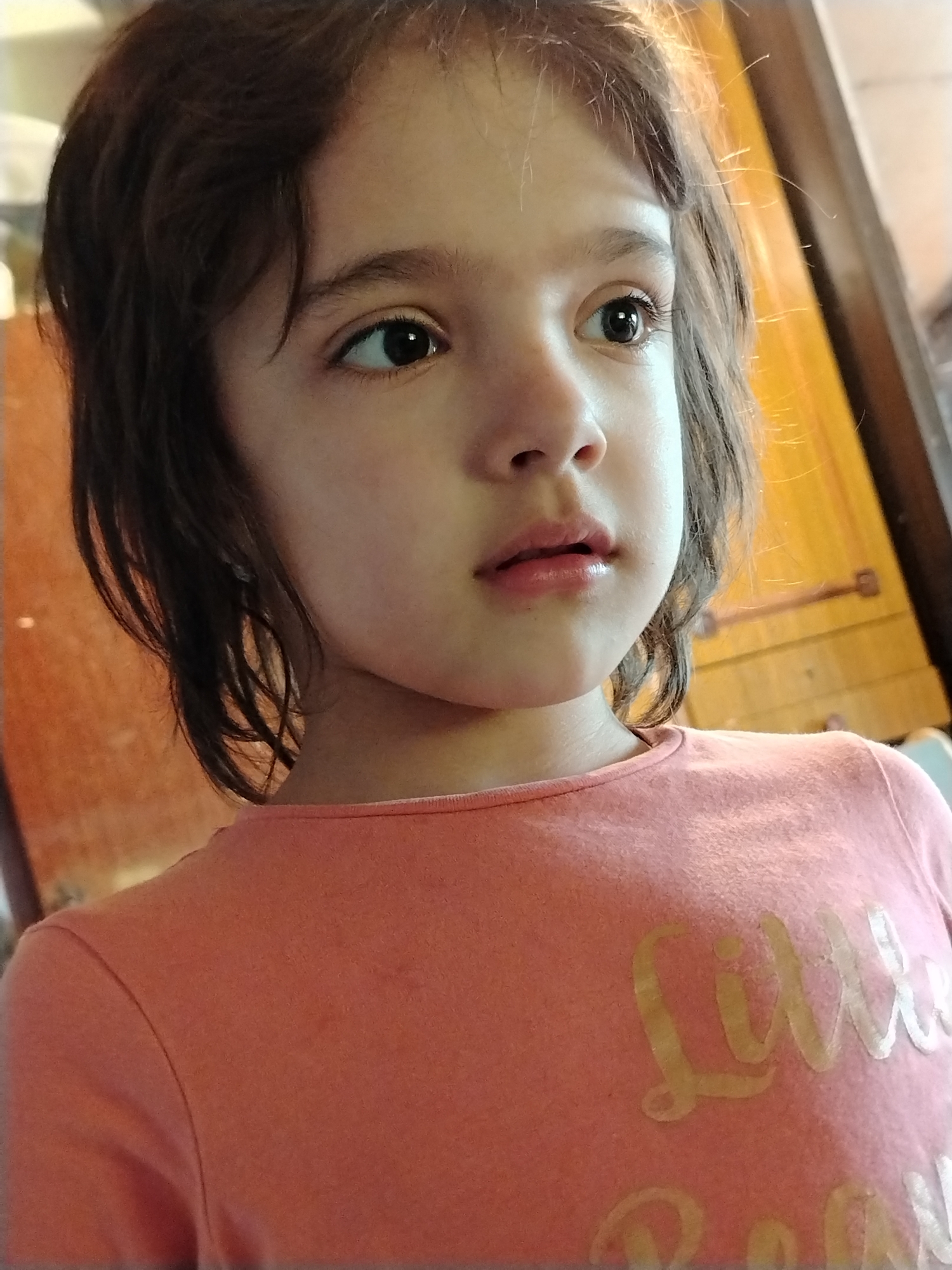 A young girl with brown hair is wearing a peach-colored shirt with the words "Little Boss" printed on it. She is looking off to the side. The location is not discernable from the image.