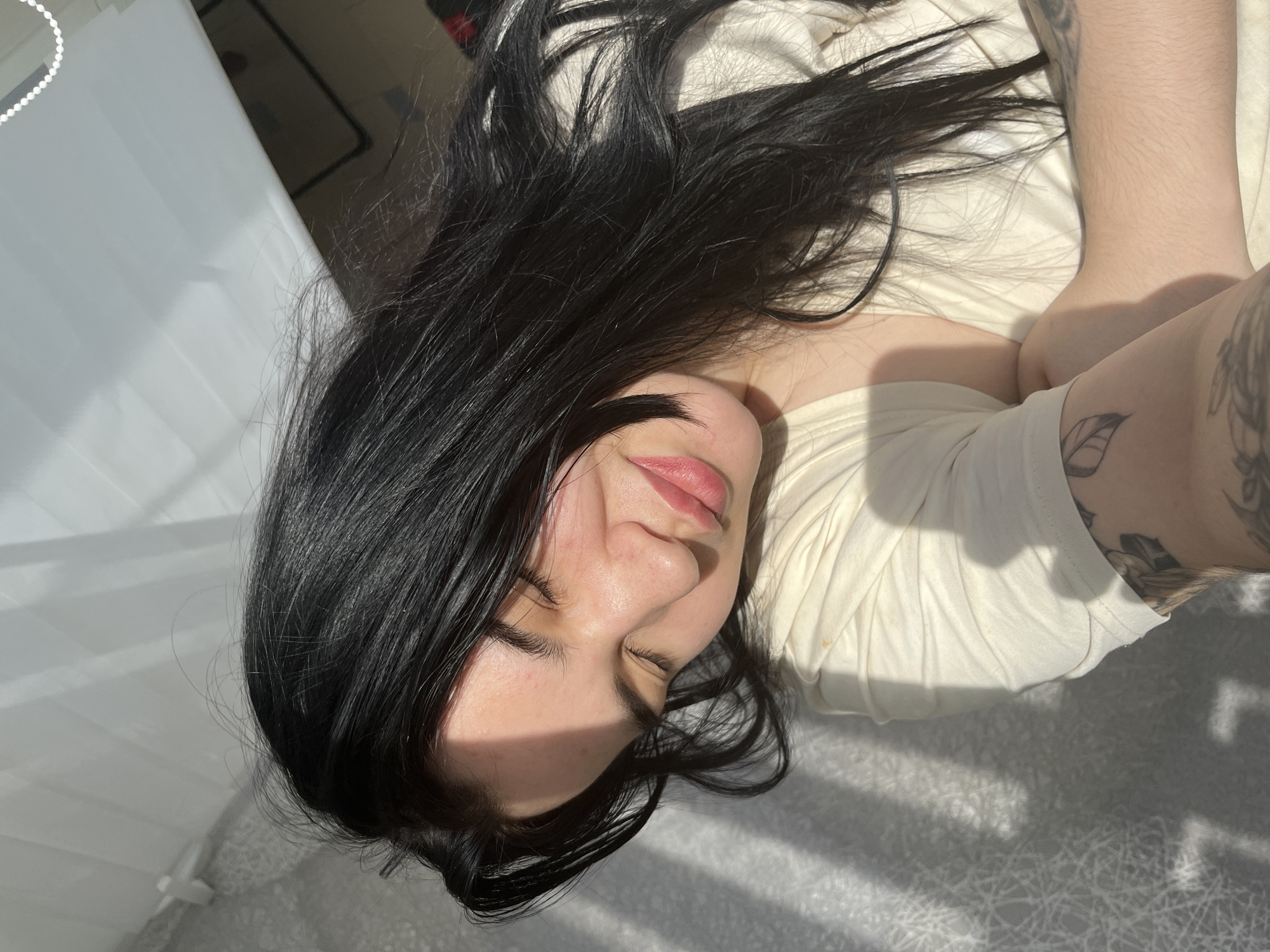 A woman with long, black hair is lying down on a bed. She is wearing a light-colored shirt. The light is creating shadows across her face and the bedding. The location is likely indoors, possibly in a residential setting. No specific details relate to the city of Chaikovsky, Russia.