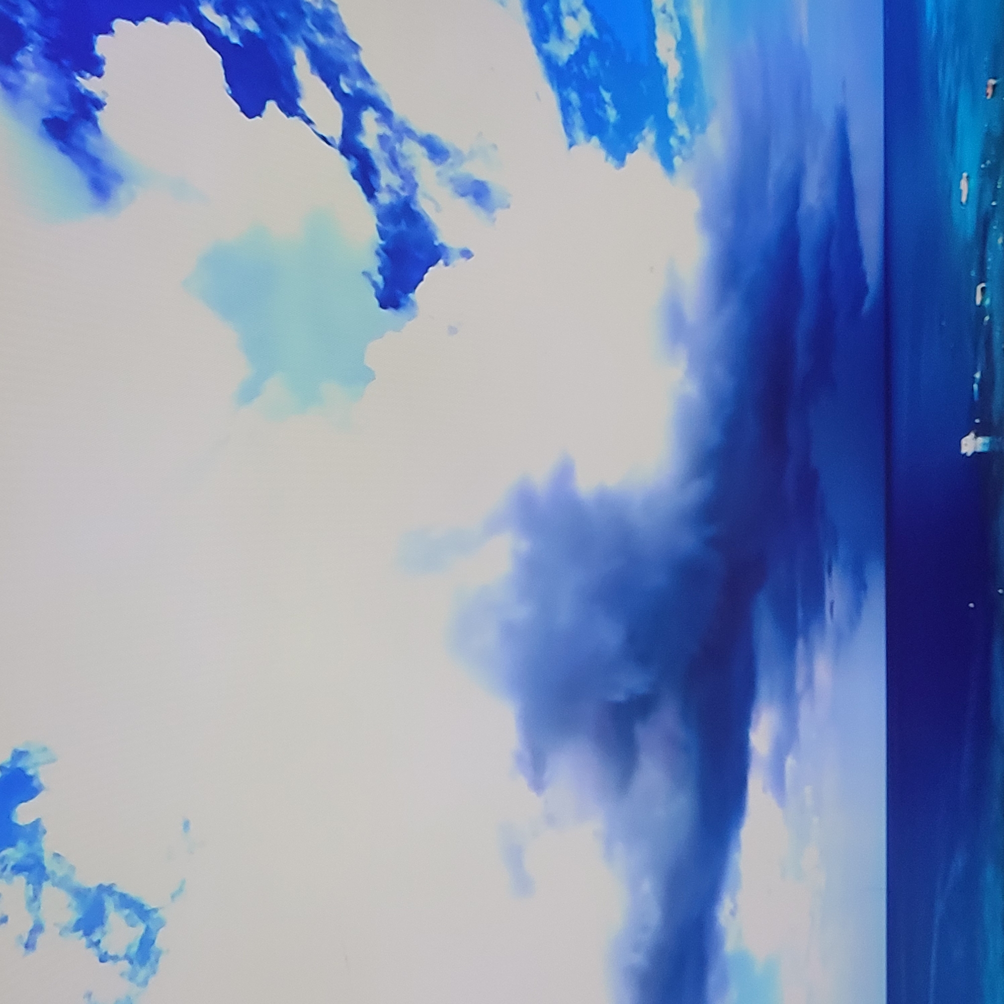 The image shows a sky scene with clouds. The clouds are primarily white with blue and gray hues. The scene is adjacent to a body of water, potentially the sea or a large lake, as suggested by the blue reflection on the far right edge. The presence of light patches within the clouds indicates illumination, possibly from the sun. There are no visible people or objects definitively identifiable as originating from Yerevan, Armenia. There is no activity that can be determined.