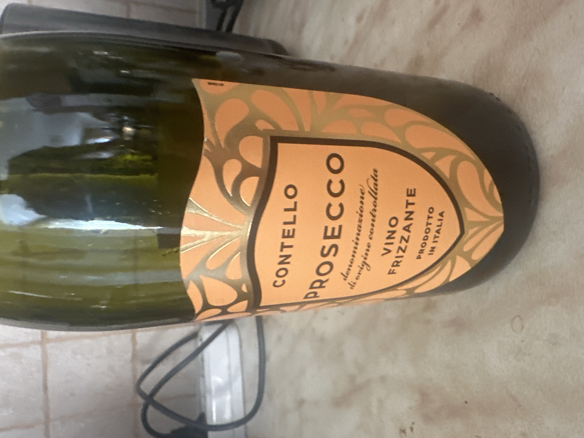 The image shows a bottle of "Contello Prosecco Vino Frizzante," a sparkling wine from Italy. The bottle is green glass with an orange label. The label indicates "denominazione di origine controllata" and "prodotto in Italia." The wine is likely lying on a light-colored surface. There is no information available to indicate that the location is Sofia, Bulgaria, or to describe any people, actions, or interactions.