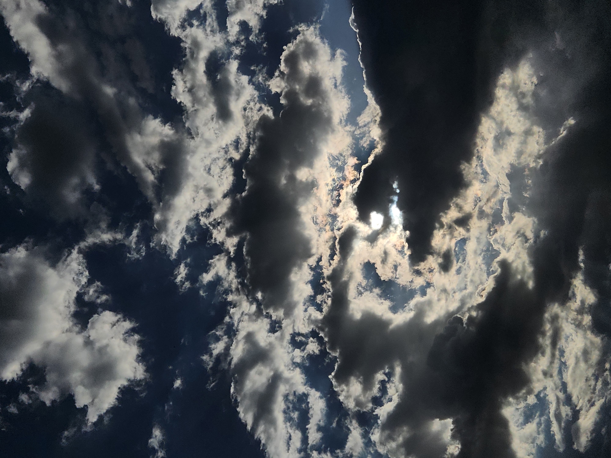 The image captures a dramatic sky filled with dark, ominous clouds interspersed with patches of bright sunlight. The clouds are thick and textured, with some appearing light and fluffy while others are dense and shadowed. The sunlight breaks through in places, creating a sense of depth and dynamism. The sky is a deep blue, providing a stark contrast to the white and grey clouds. There are no people, subjects, objects, or actions visible in the image; it is a purely atmospheric landscape. The specific location in Maitland, United States of America, is not discernible from the visual information provided.