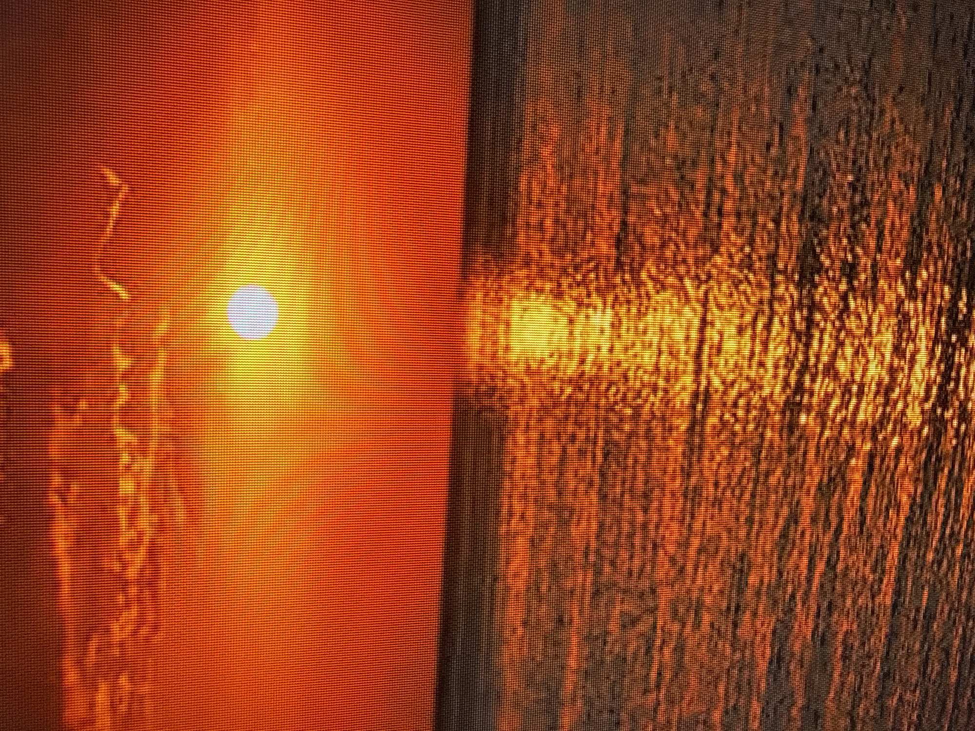 The image depicts a sunset over a body of water. The sky is a vibrant orange, with some hazy clouds visible. The sun, a bright white orb, is positioned in the upper center of the frame, casting a strong reflection on the water's surface. The water is textured with ripples, and the reflection of the sun creates a shimmering path of light extending from the horizon towards the viewer. The overall scene is one of natural beauty and tranquility. There is no discernible city or specific location identifiable within the image, and therefore, no connection to Szczecin, Poland can be made. The image contains no people, subjects, objects, actions, or interactions.