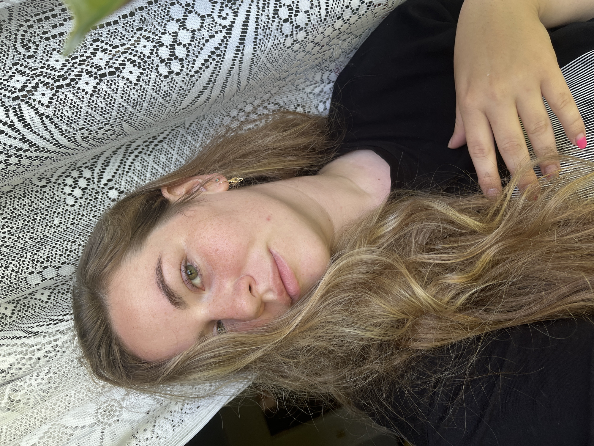 A woman with light blonde hair lies on a surface covered with white lace. She is wearing a black top and has one nail painted pink. The location is Сосново, Russia.