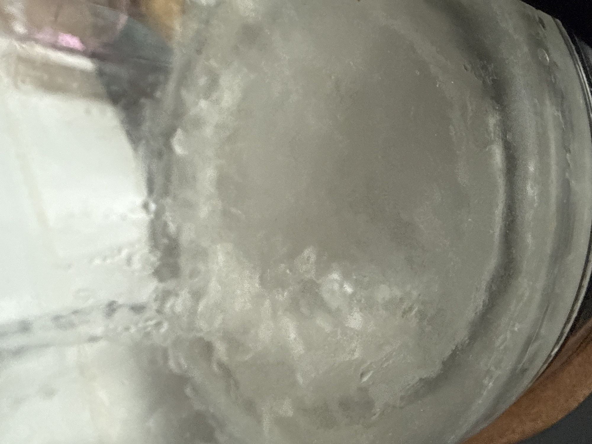 A close-up shot shows the interior of a glass container, possibly a jar or bottle. The contents appear opaque, white or light gray, and somewhat textured or cloudy. The texture suggests it might be a suspension, emulsion, or a material with small particles. On the left, the glass is more transparent with a blurred reflection of something outside the jar, hinting at a liquid-air interface. The light source is likely external and illuminates the contents of the container from various angles, producing shadows and highlights within the opaque substance. The scene is photographed from a perspective looking directly into the open top of the container, which is somewhat distorted due to the curvature of the glass. There is no evidence in this image to connect the shot with the city of Vidnoye in Russia.