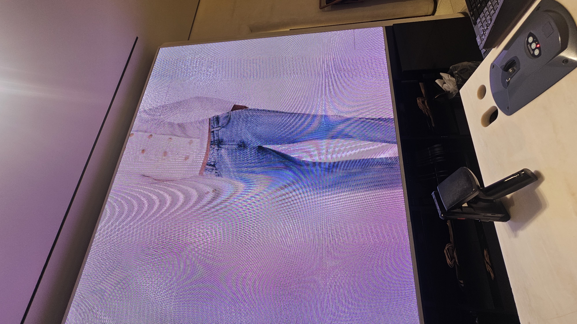 The image shows a screen displaying an image with color distortion, positioned next to a desk with a keyboard, a device with buttons, and a stapler. The location is Puebla, Mexico. The environment appears to be indoors.