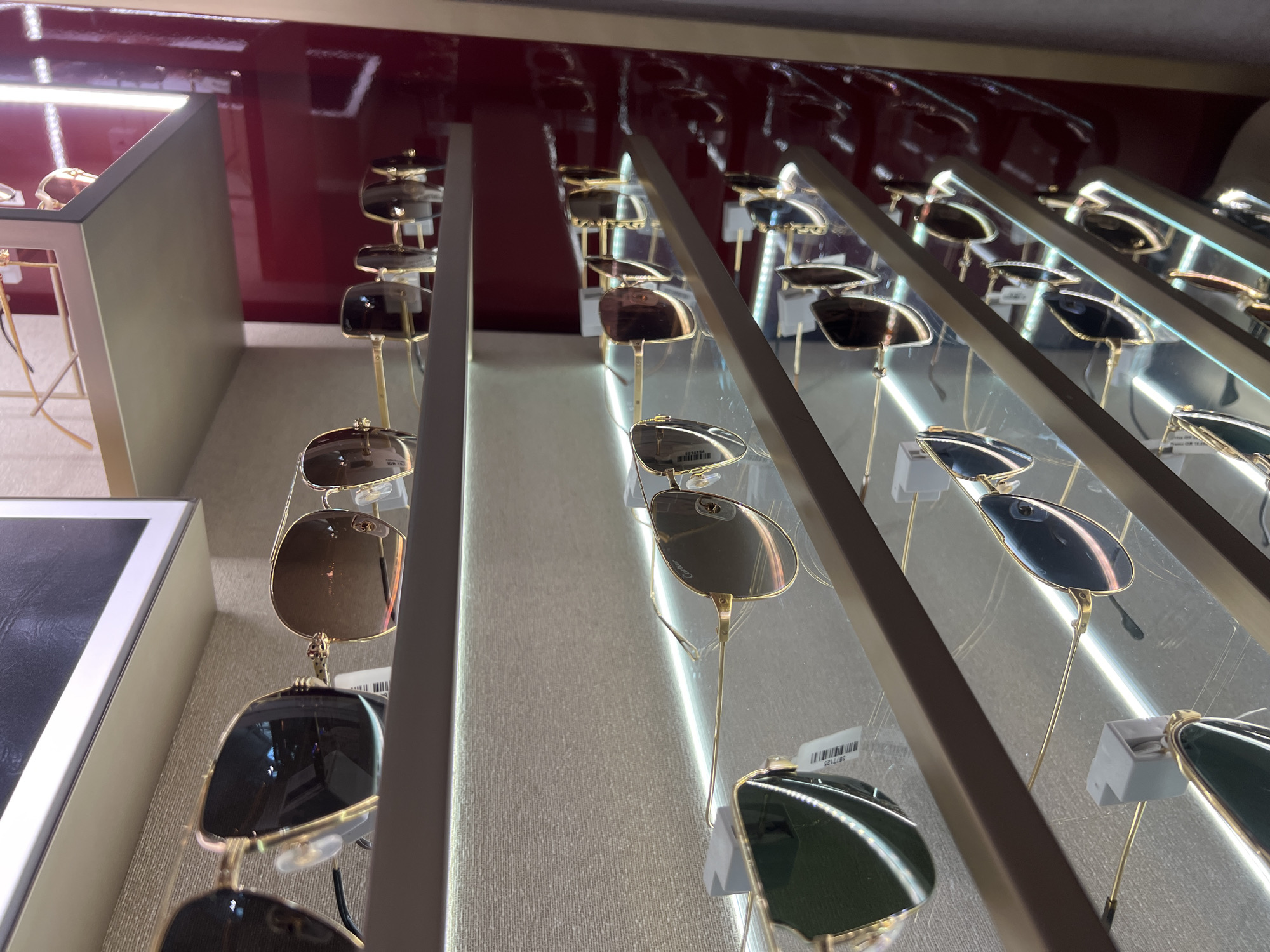 A display of sunglasses in Kuta, Indonesia shows several rows of glasses on individual stands. The frames are arranged in a diagonal line, receding into the background, with a red back wall. The sunglasses feature various colors and lens shapes.