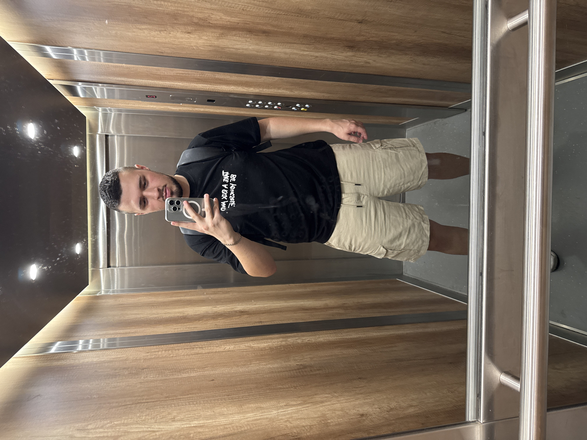 A man is taking a selfie in an elevator. The elevator has wood-paneled walls and a gray floor. Elevator buttons are visible on the back wall. The location is likely Sofia, Bulgaria.