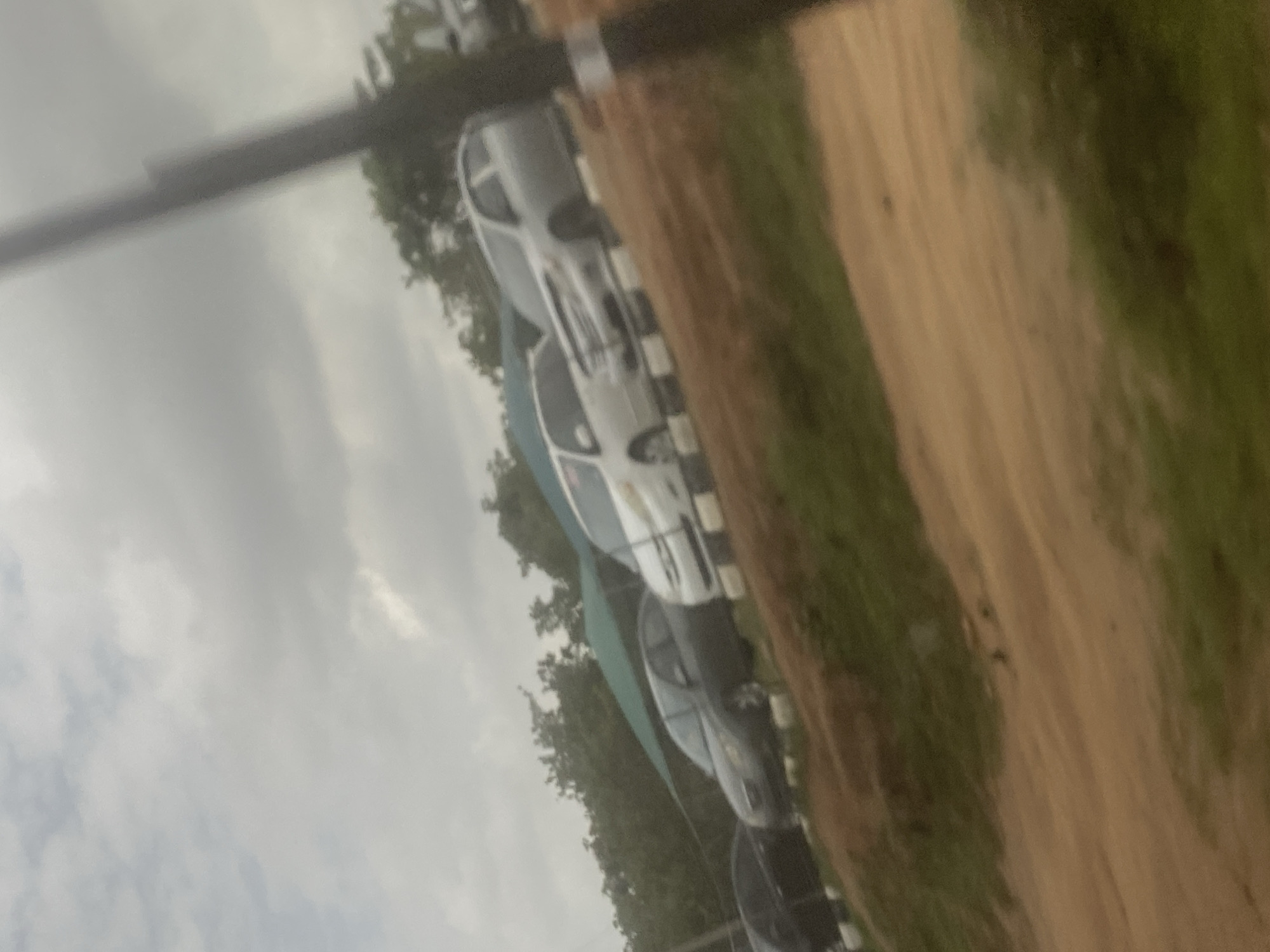 The image shows a row of cars parked next to a dirt road. The sky is overcast. The location cannot be determined as Abuja, Nigeria without additional information or visual cues specific to the area.