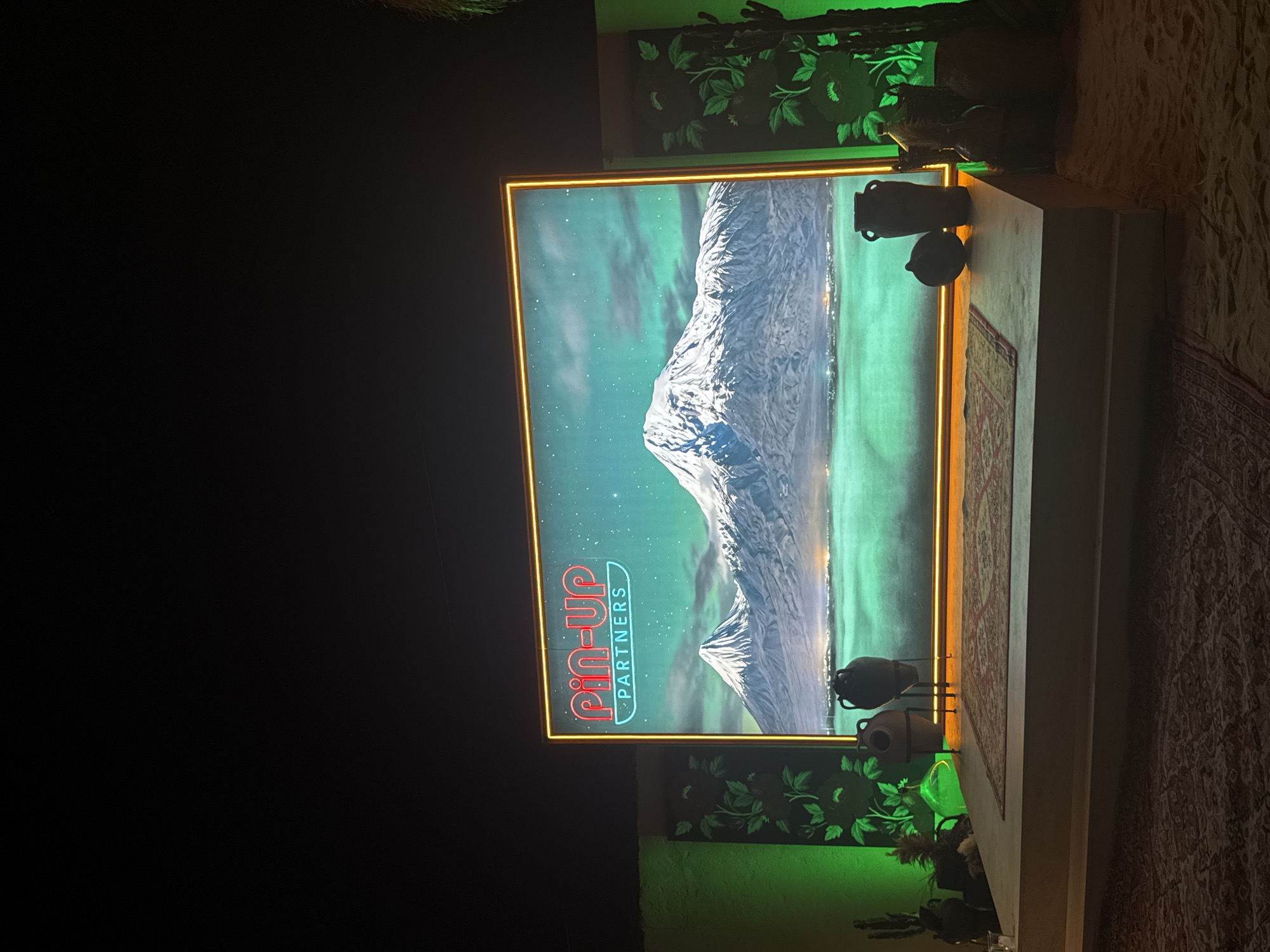 The image shows a display featuring a neon sign for "Pin-Up Partners" with a landscape of Mount Ararat in the background. The display includes decorative urns, a carpet, and floral artwork. The location appears to be Parakar, Armenia, given the depiction of Mount Ararat.
