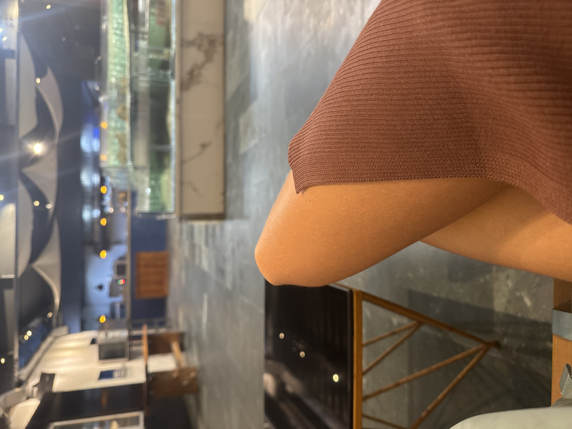 An indoor scene shows crossed legs and a brown knit garment. The setting appears to be a restaurant or similar establishment, with tables, seating, and decorative lighting visible in the background. The location is suggested to be Đà Nẵng, Vietnam, based on the style and ambiance of the place, but without additional landmarks or signs, this cannot be definitively confirmed.