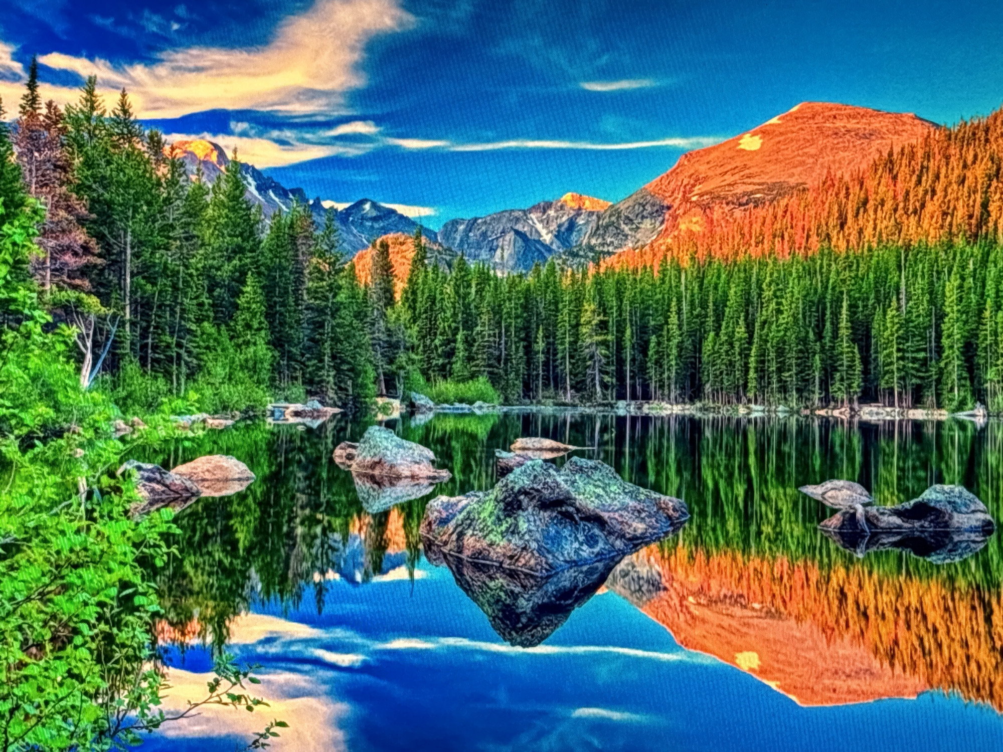 This is a hyper-realistically rendered, high-dynamic-range photograph of a pristine mountain lake reflecting a vibrant sky and a dense evergreen forest. The foreground features lush green foliage on the left, with several large, textured rocks emerging from or floating on the calm, glassy surface of the lake. In the background, a majestic mountain range is bathed in warm, orange sunlight on its peak, contrasting with the cool blue of the sky and the deep green of the surrounding pine trees that line the far shore. The water's reflection is almost a perfect mirror image of the scene above, creating a sense of depth and symmetry. The location is not identifiable as being in the city of Sofia, Bulgaria, as the landscape depicts a wild, natural mountainous terrain.