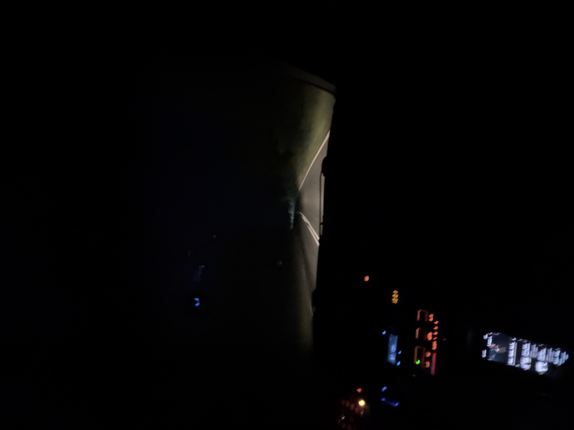 The image depicts a night scene, likely from inside a vehicle moving on a road near Cherni Vrah, Bulgaria. A dimly lit road is visible through the windshield, with a grassy area to one side. The interior of the vehicle is visible in the foreground, including the dashboard with illuminated displays and controls. No people are clearly visible. The environment appears to be rural or sparsely populated, given the darkness and lack of prominent urban features. The main action inferred is the movement of the vehicle on the road at night.