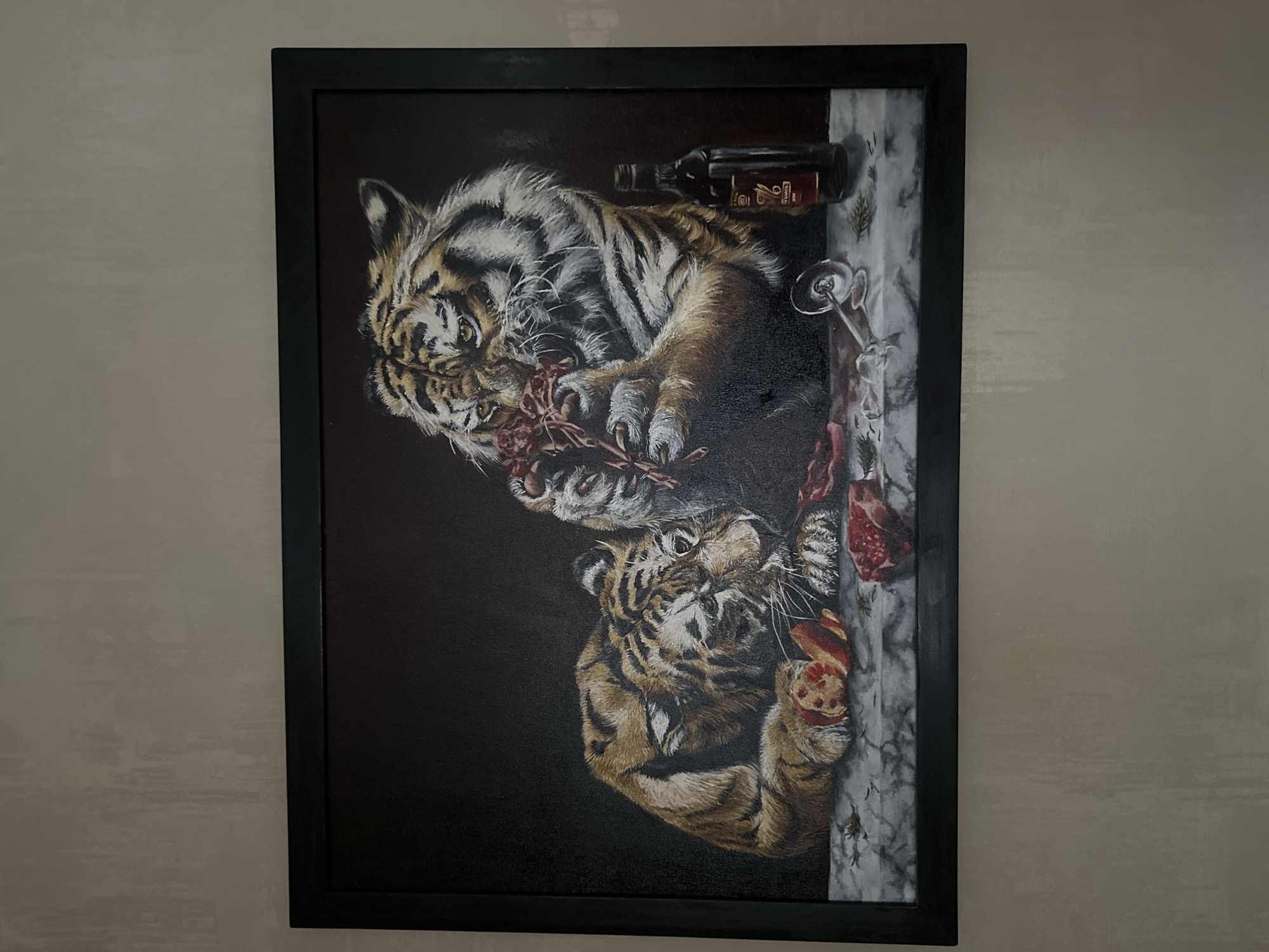 A framed painting hangs on a wall. The painting depicts two tigers, one above the other, eating raw meat. Above the upper tiger is a wine bottle and a partially filled wine glass. The right side of the painting has a marbled surface with more pieces of raw meat, and some herbs. The background of the painting is black. The location is not specified.