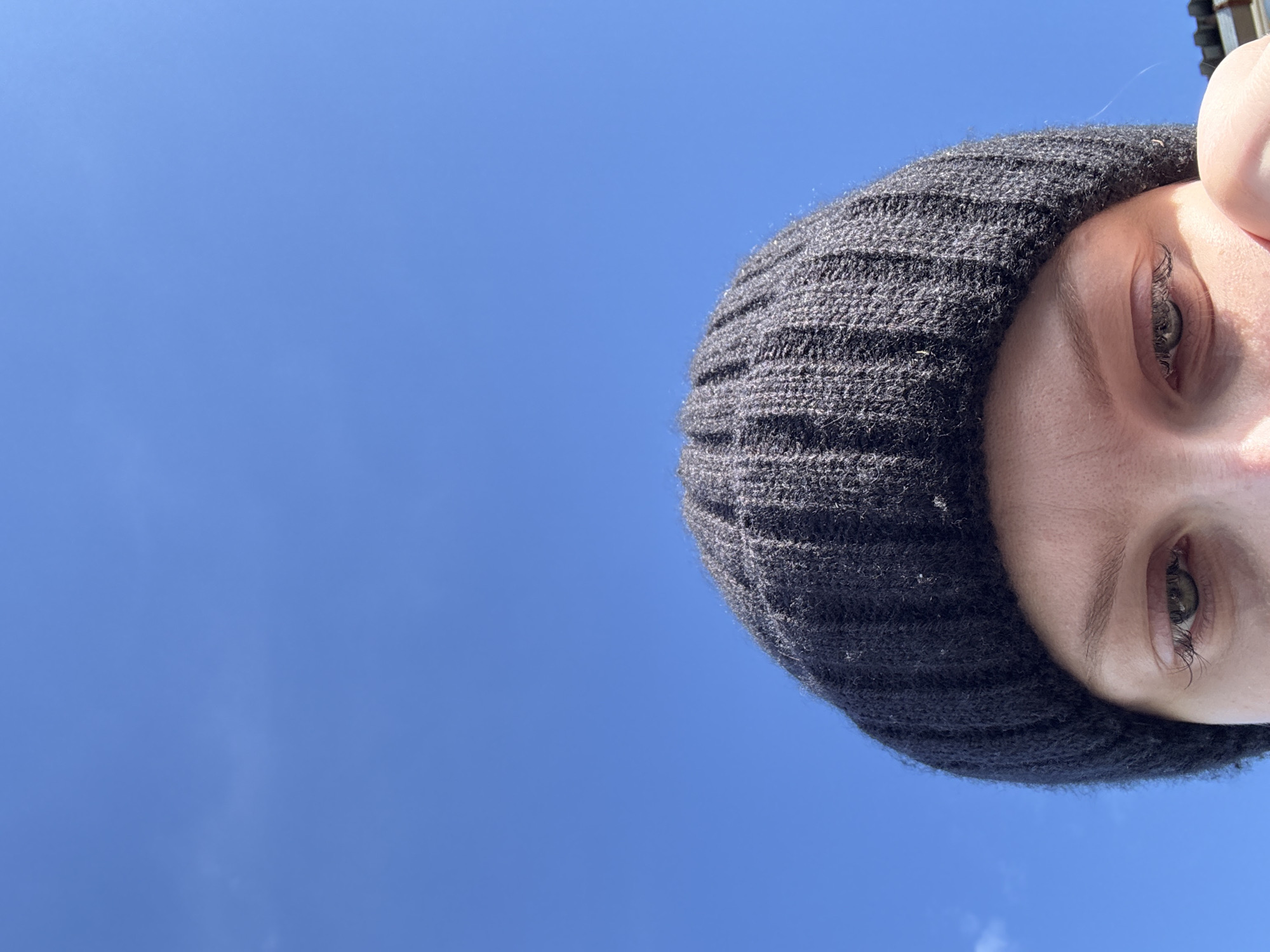 A low-angle shot shows a person wearing a black knit beanie against a bright blue sky. The person's face is partially visible, focusing on their eyes. The exact location in the city of Бородулино, Russia, cannot be determined from the image.