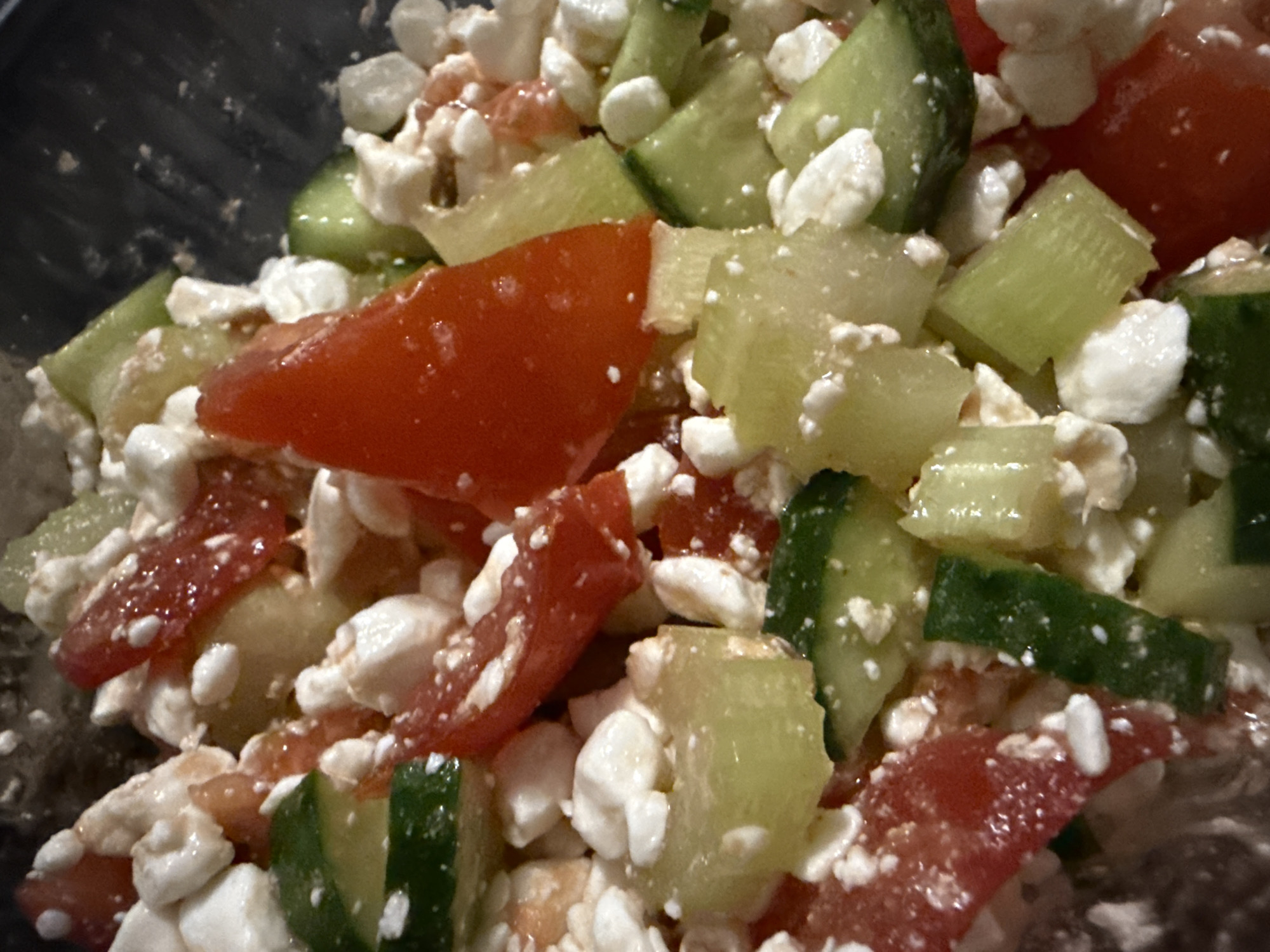 The image depicts a close-up of a salad composed of diced cucumbers, chopped tomatoes, and crumbled feta cheese. There is no evidence to suggest the location is Chaikovsky, Russia, nor are there any people or actions visible in the image. The environment appears to be indoors, likely a bowl or container holding the salad.
