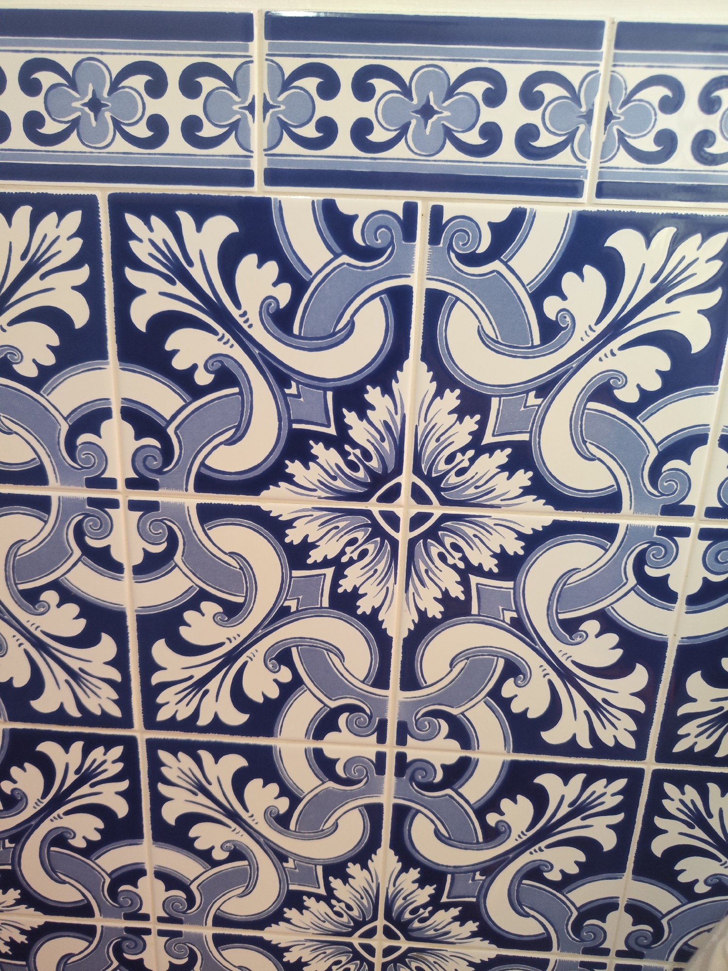 The image depicts a section of a tiled wall featuring a blue and white patterned design. The primary design consists of repeating squares, each adorned with stylized floral and swirl motifs in shades of blue and white. The tiles at the top of the frame feature a different pattern: a horizontally oriented strip with a floral design and blue stripes. The tiles are clean and appear to be in good condition. The specific location of Ribeira Grande, Portugal cannot be confirmed without further contextual information.