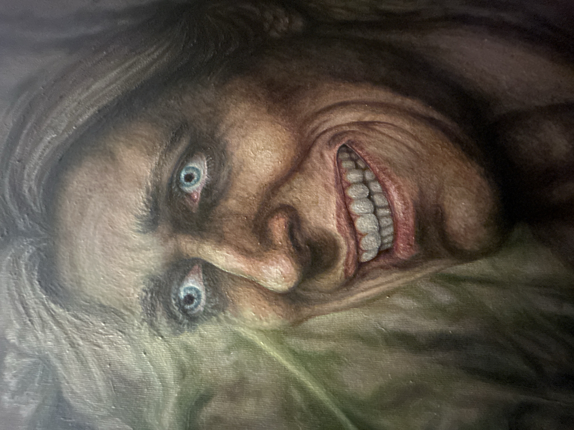 The image is a close-up painting of a person's face with an unsettling expression. The person has pale skin, gaunt features, and light hair. Their eyes are wide and blue. The mouth is open in a wide, toothy grin, with visible gums. The painting appears to be done in a realistic, albeit somewhat distorted, style. The background is indistinct and dark. There is no information available in the image to associate it with Cape Coral, United States of America.