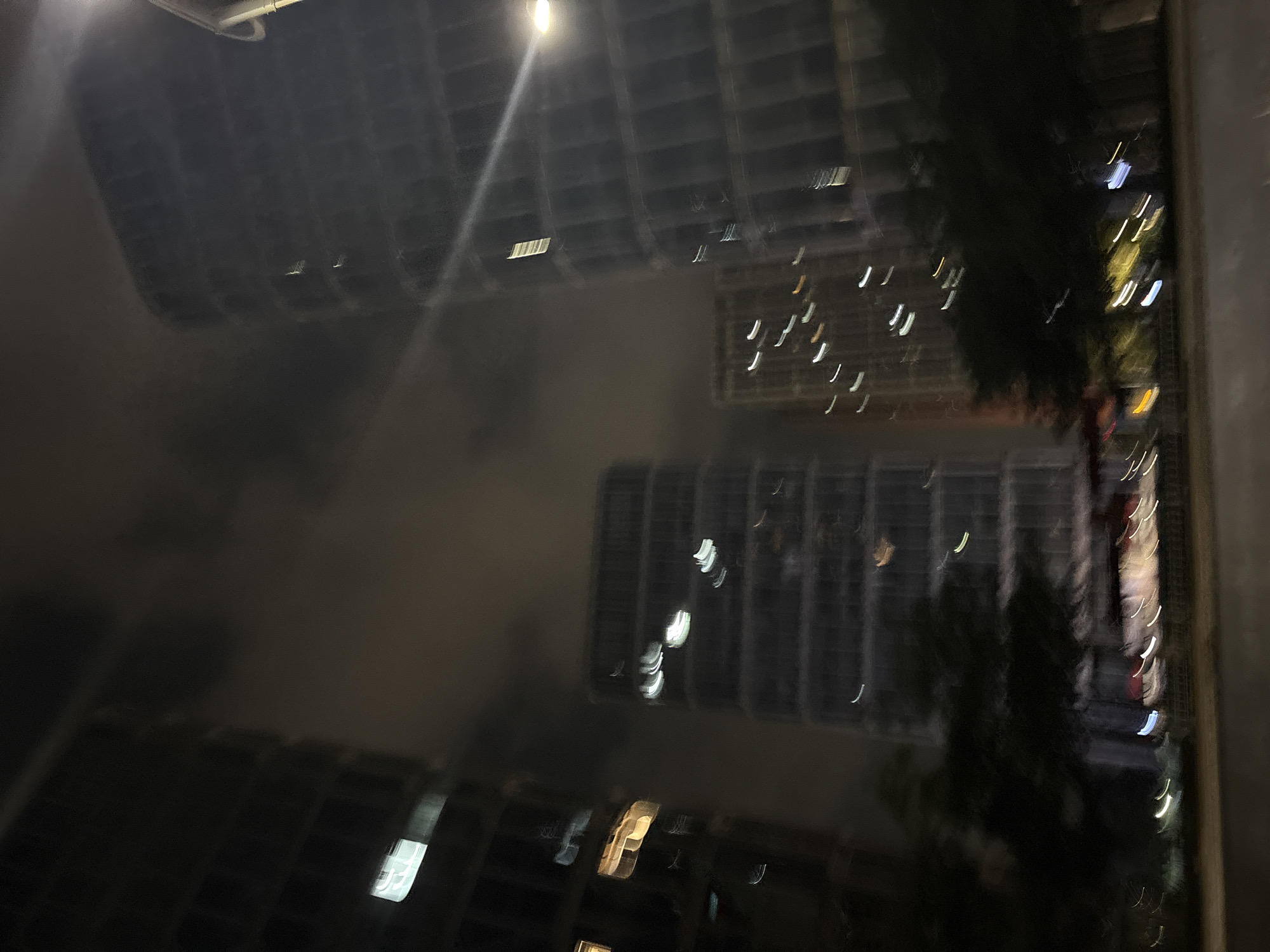The image is a nighttime photograph of a city street in Haizhu District, China. Several tall buildings, characteristic of urban environments, are visible. The buildings appear to be modern, with glass facades that reflect the city lights. The photograph is taken from a low angle, looking up at the structures. The street in the foreground is paved and appears wet, suggesting recent rain or a reflection of the overhead lights. Some trees are present along the side of the street, their dark silhouettes contrasting with the illuminated buildings. The overall impression is one of a dynamic, modern city at night, with streaks of light from vehicles or streetlights adding to the atmosphere.