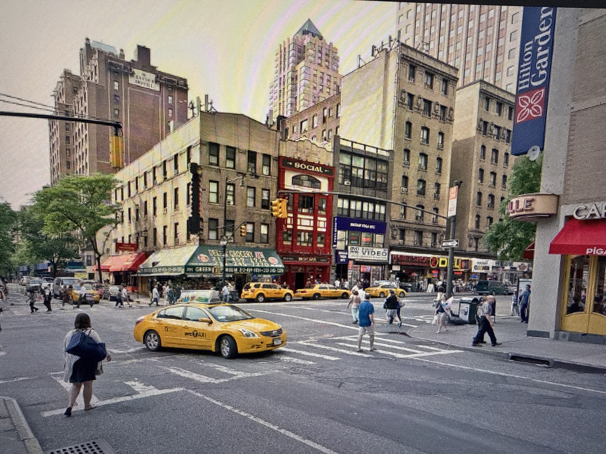 This image shows a busy street scene in New York City. Yellow taxis are prominent, and people are crossing the street at a crosswalk. Tall buildings are in the background. A Hilton Garden Inn banner is visible. There's a cafe with a red awning on the right. The sky is overcast. The Sofia, Bulgaria portion of the request is not consistent with the image.