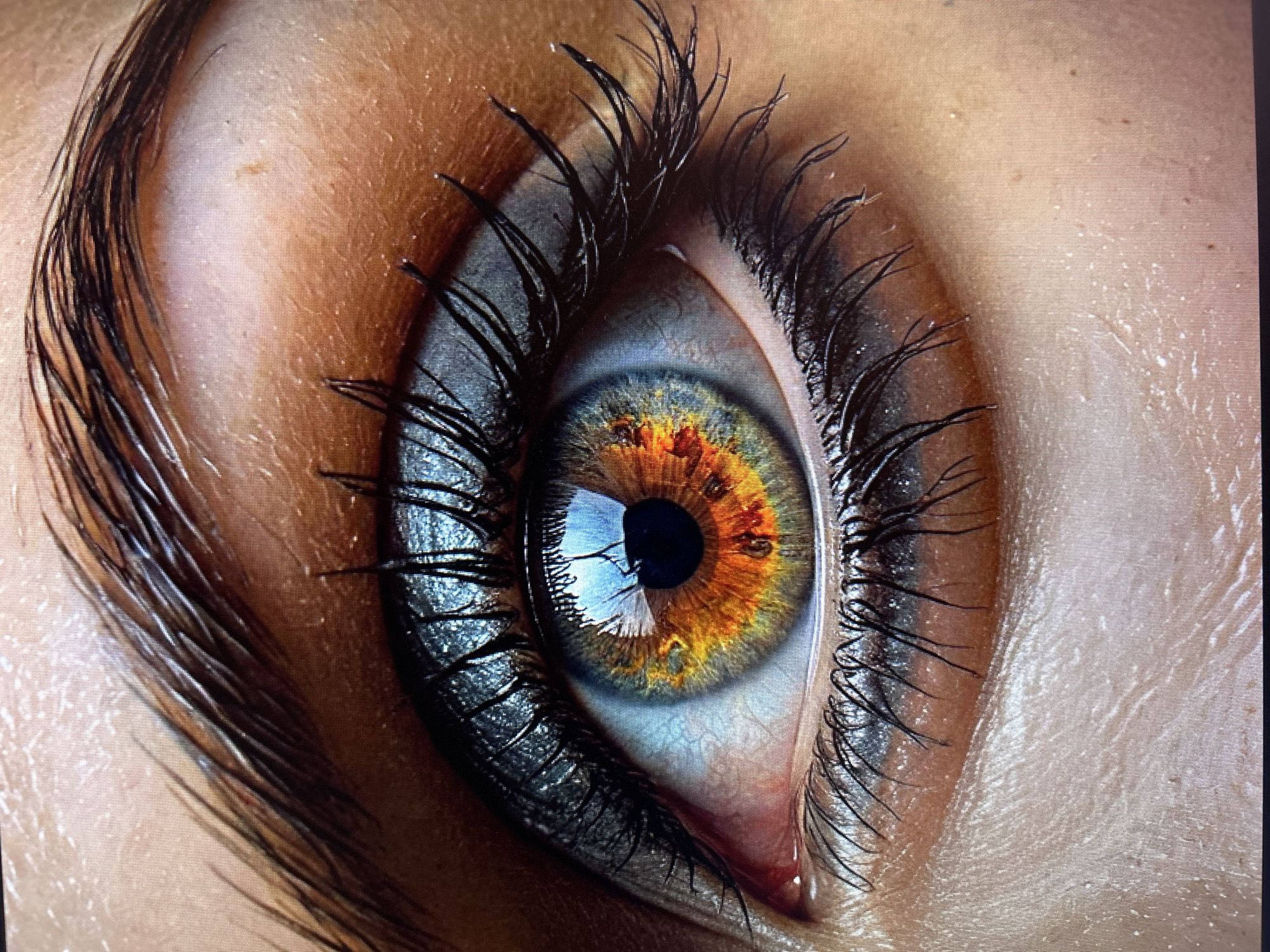 A close-up shot showcases a person's eye, meticulously detailed. The iris is a striking blend of blues, greens, and fiery oranges, creating a mesmerizing pattern. Thick, dark eyelashes frame the eye, enhanced by dramatic eye makeup. The skin surrounding the eye is rendered with incredible texture, highlighting pores and subtle variations in tone. The lighting in the image is intense, reflecting off the eye and makeup, adding to the overall dramatic effect. The specific location of this eye in the city of Unknown, Unknown is not discernible from the provided image.