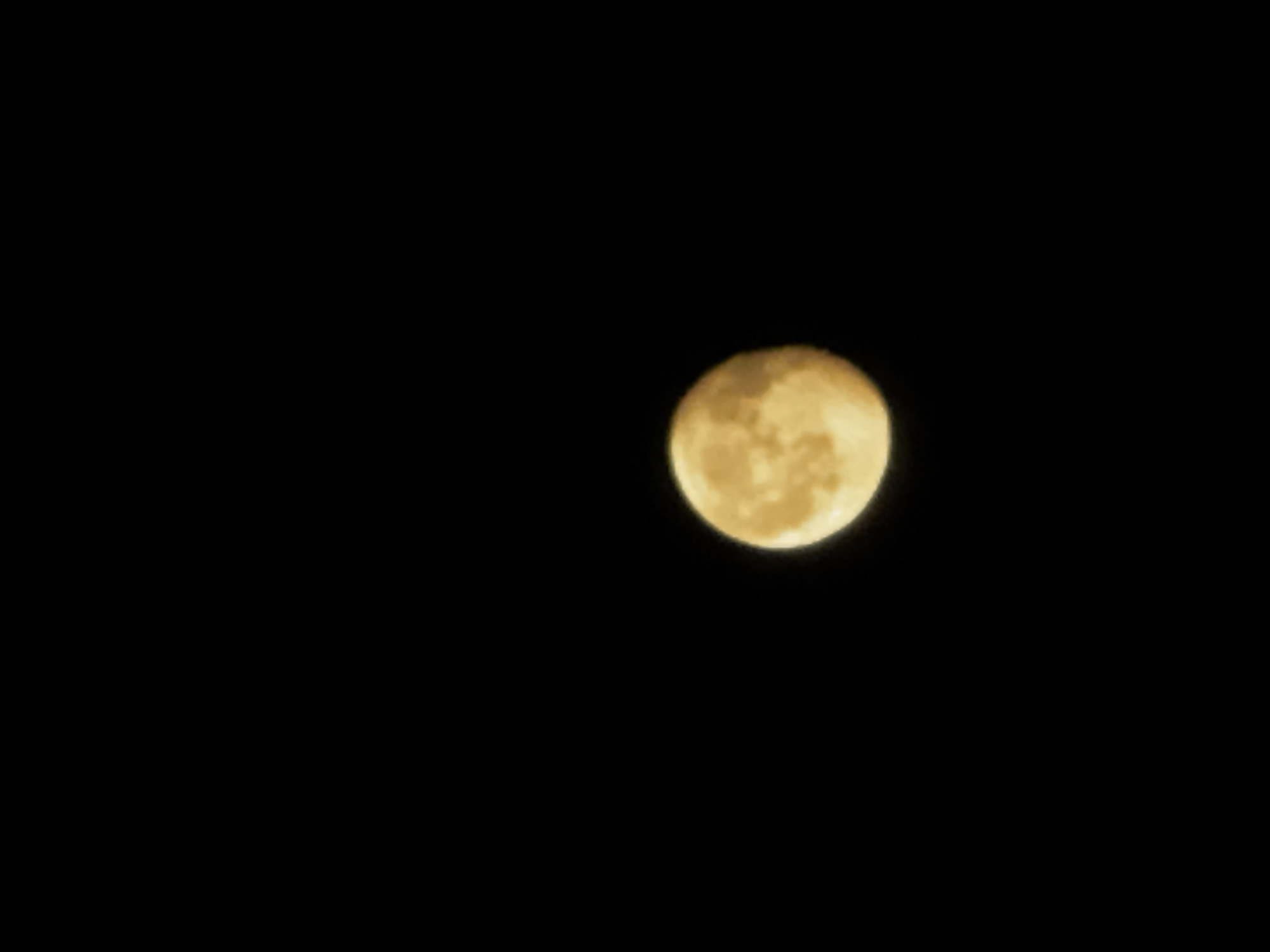 A full moon is visible in a black sky. The moon is round and a pale yellow color with some darker markings visible on its surface. The image appears to be a photograph taken at night. The location in the city of Dubna, Russia is not specified in the image.