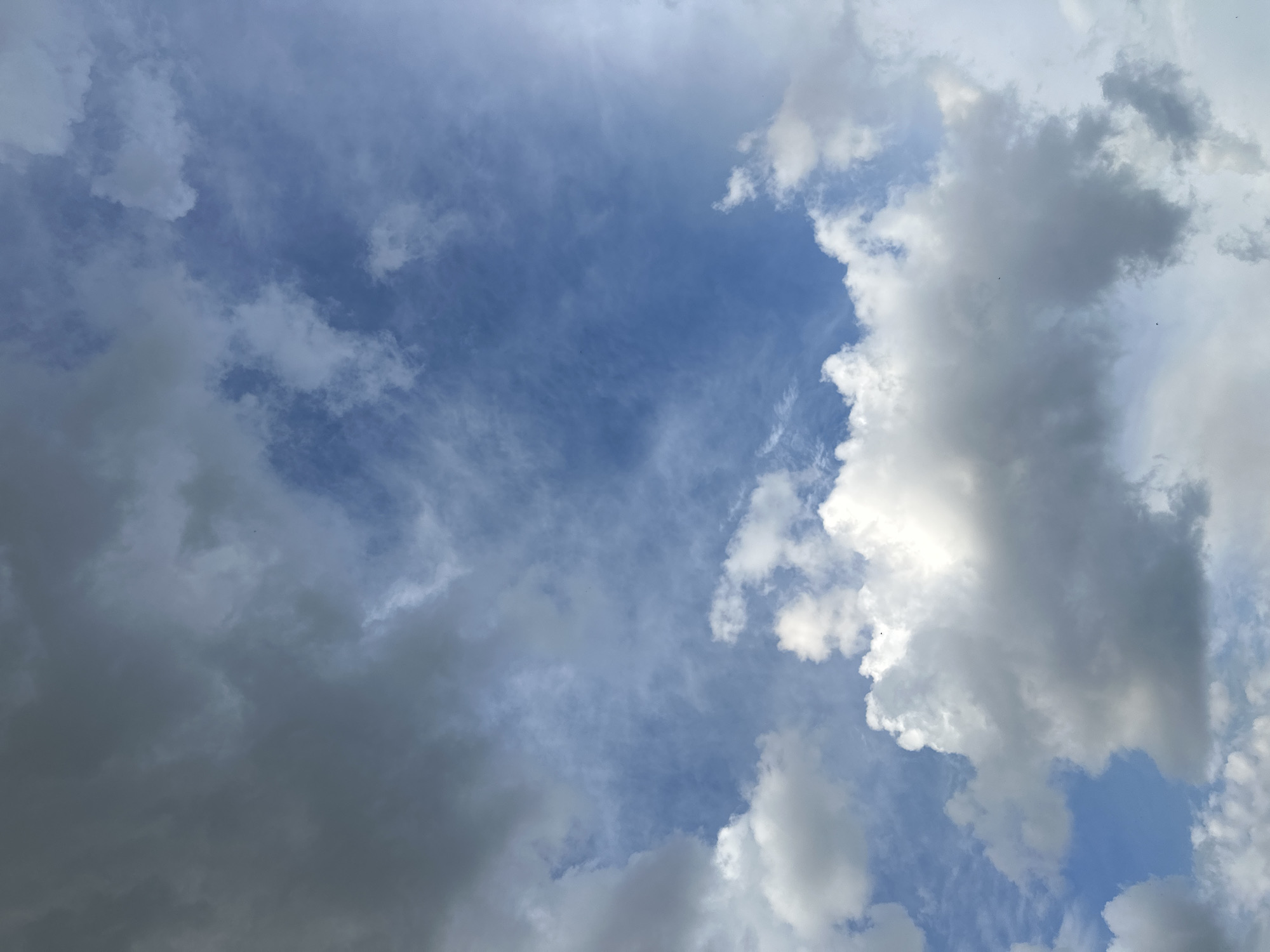 The image displays a vast expanse of the sky over Magnitogorsk, Russia. A mix of dark, overcast clouds occupies the upper left quadrant, transitioning into a brighter, partly cloudy sky towards the right and bottom. The blue sky is visible in patches, interspersed with various formations of white and gray clouds. Some clouds are thin and wispy, while others appear dense and voluminous, suggesting potential for rain or varying weather conditions. The scene is devoid of any visible structures, people, or specific landmarks within the city. The focus is solely on the atmospheric conditions and the sky itself.