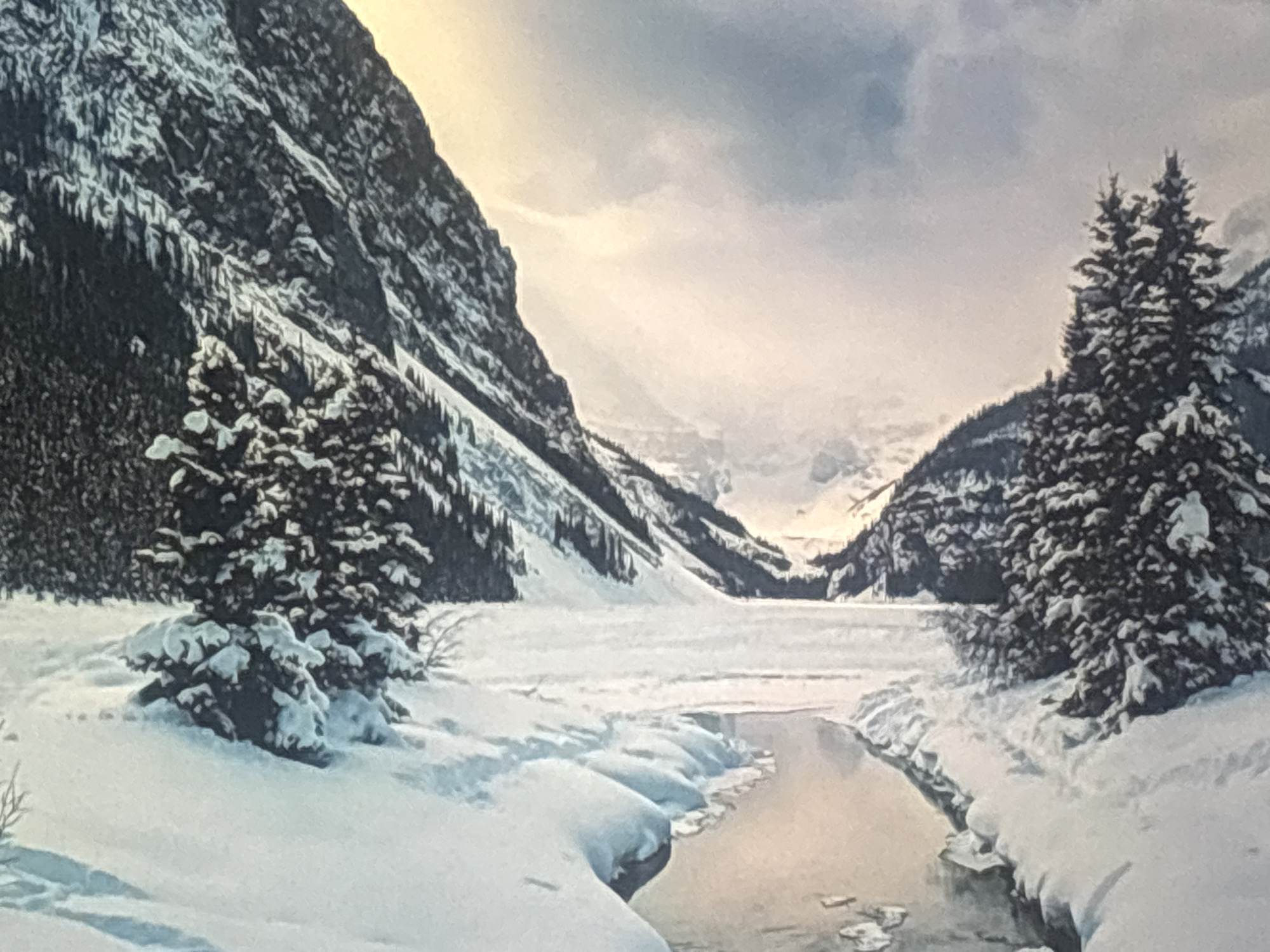 This is a painting of a snowy mountain landscape. The scene depicts a narrow, partially frozen stream flowing through a valley. On either side of the stream are snow-covered banks, and beyond them, snow-laden evergreen trees. The valley is enclosed by steep, dark mountainsides, also covered in snow and trees. The sky above is cloudy and pale, with hints of warm light suggesting either sunrise or sunset. The overall impression is one of serene, winter beauty and a remote, natural setting. The painting does not contain any people, objects, or visible text. The location context of Valladolid, Spain, is not reflected in the imagery of the painting, which appears to be a mountainous region, possibly the Alps or Canadian Rockies.