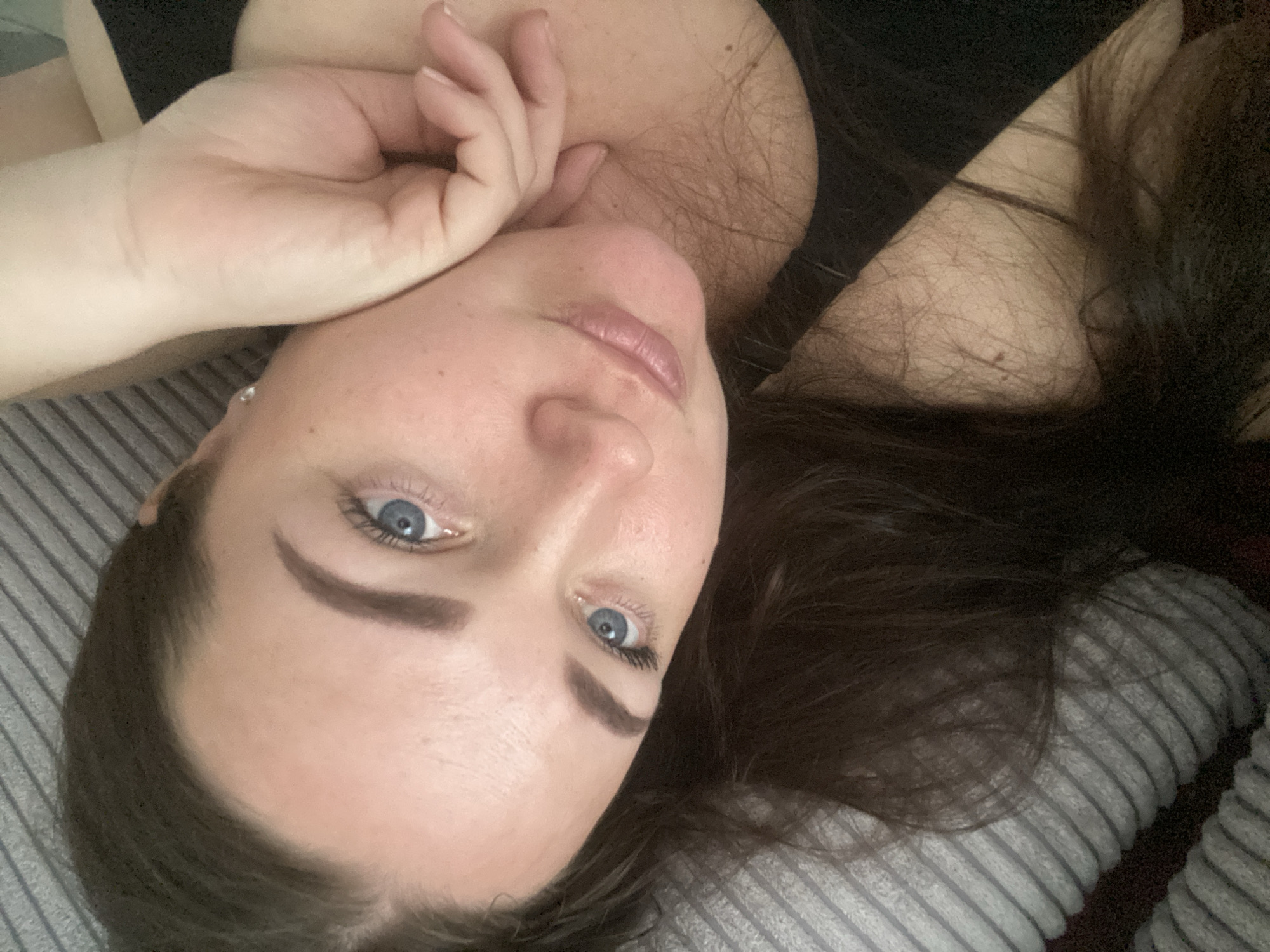 A woman with fair skin, blue eyes, and dark brown hair is lying down. Her head is tilted to the side. She is resting her left hand near her face. The background shows a striped surface, possibly a pillow or bedding. The top of her shoulder is visible. The image is taken indoors. The city of Sochi, Russia, is not discernible from this image.