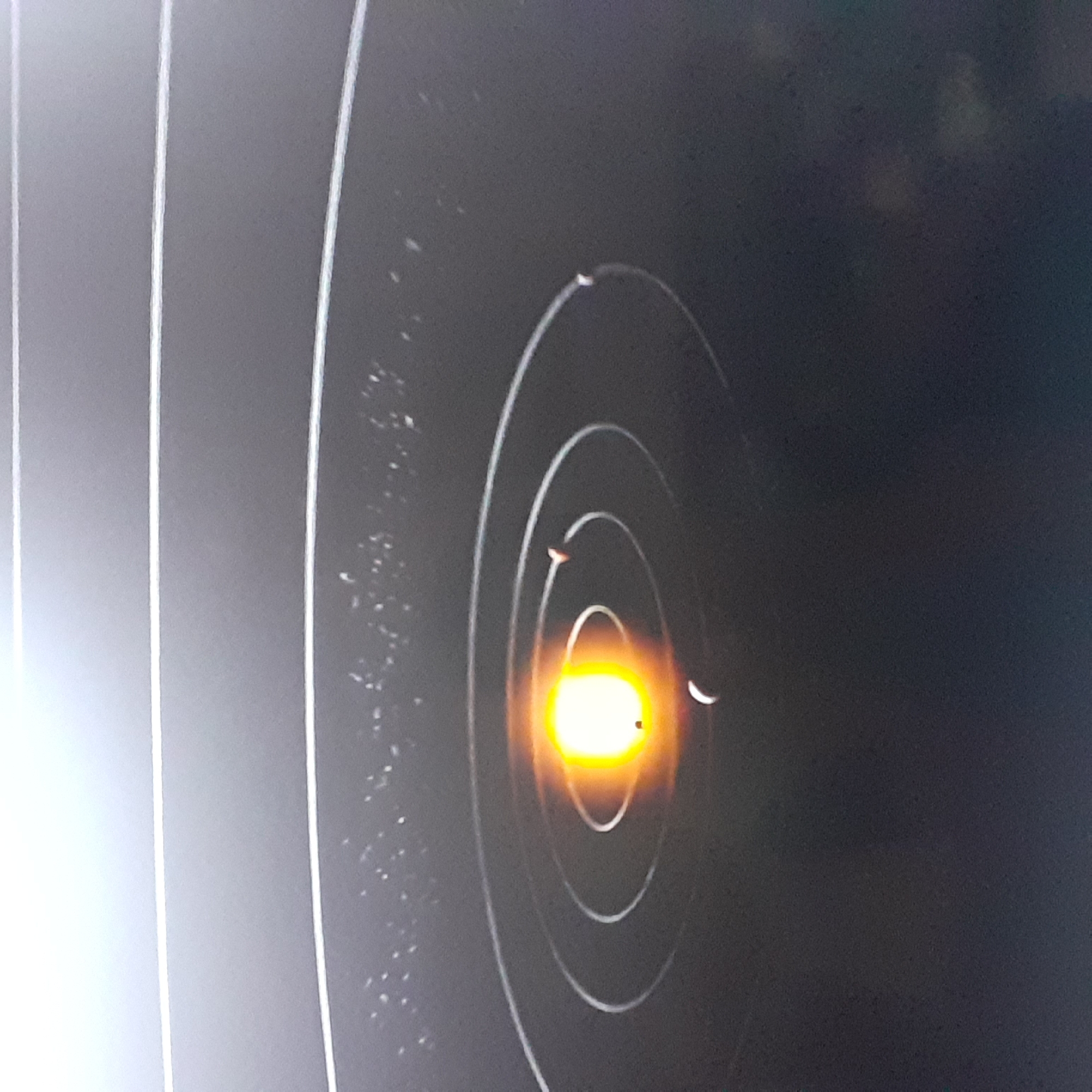 A close-up shot of a target with concentric circles, presumably for shooting practice. There are visible bullet holes on the target, particularly clustered around the center bullseye, which is brightly illuminated. The surrounding areas appear dark, possibly indicating an indoor or dimly lit shooting range. The image does not contain information regarding Sofia, Bulgaria. No people are visible.