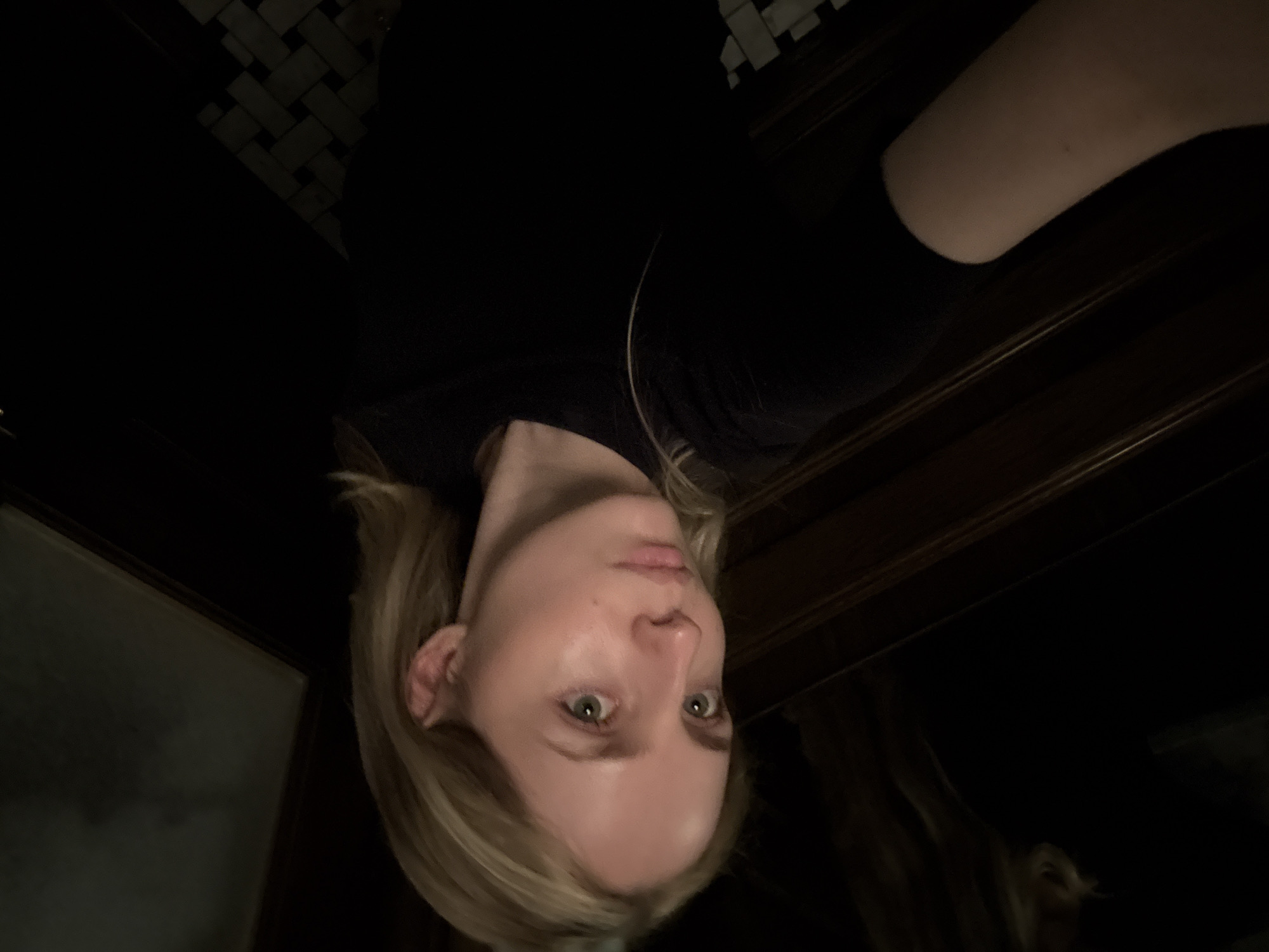 The image shows a light-skinned person with blonde hair and green eyes. They are wearing a dark-colored shirt. The background includes what appears to be a dark wooden surface or furniture, as well as a section with black and white patterned tiles. There is no additional information to determine the location in Mexico City, Mexico.