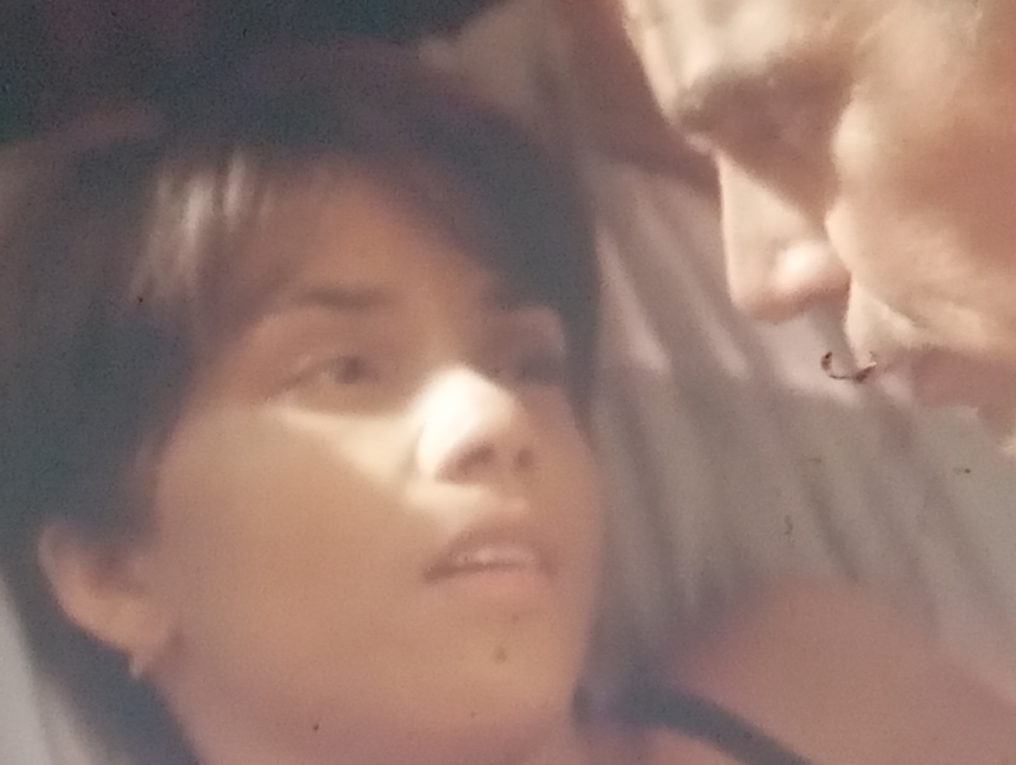 The image is a close-up, slightly blurry photograph of two people, their faces partially visible. The person in the foreground, on the left, appears to be a young female with dark hair and an earring. Her gaze is directed downwards and slightly to the right. The other person, on the right, is an adult with lighter-colored hair, seen in profile, looking towards the person in the foreground. The background is indistinct, with muted tones. The lighting is soft, creating a warm, intimate atmosphere. The image does not contain any information about a specific location in Sofiivska Borshchahivka, Ukraine.