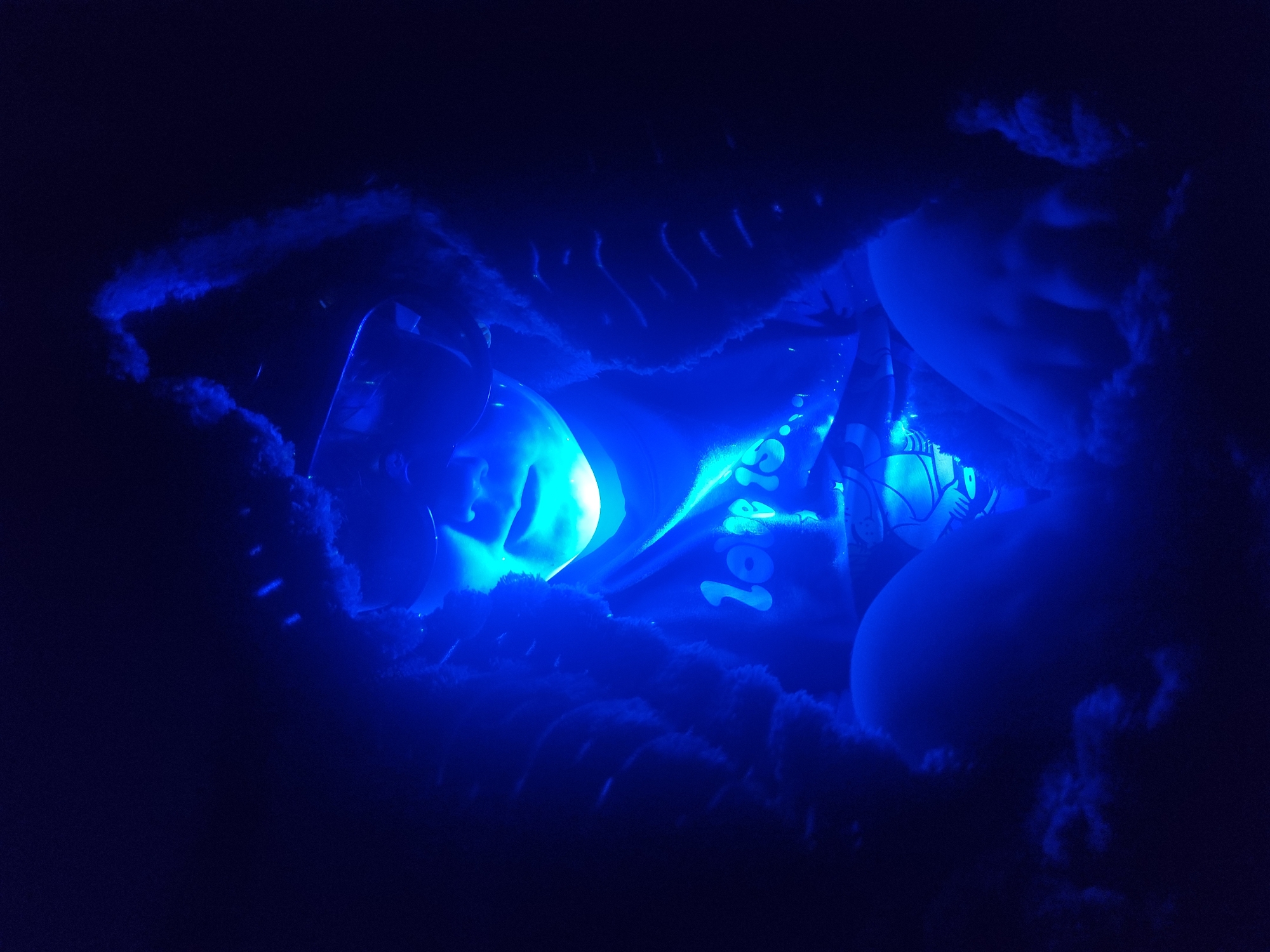 A view through a blue, fuzzy opening reveals what appears to be a child's face partially illuminated by a bright light. Balloons are also visible within the opening, along with what appears to be a banner or sign with text "Tor...", suggesting "Tort" (cake in Russian). The location and setting suggest it could be a children's party or event, possibly in Chaikovsky, Russia.
