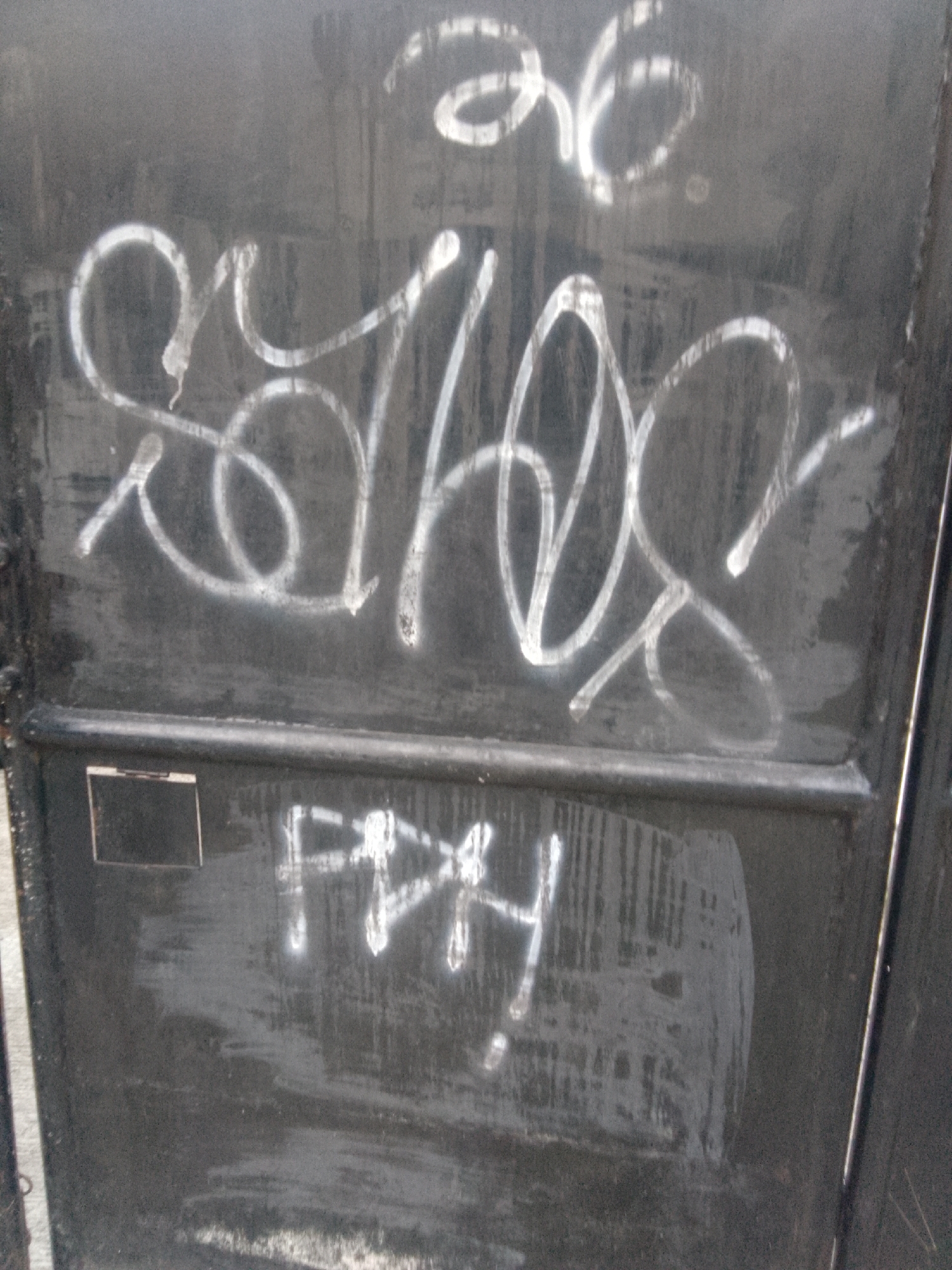 The image depicts graffiti on a dark, weathered metal surface, possibly a door or dumpster. The graffiti consists of two distinct tags. The upper tag is larger and more elaborate, rendered in white, and appears to be a stylized name or symbol. It features swirling lines, loops, and what may be the numbers "36" incorporated into the design. Below this, a smaller, cruder tag in white reads "FPHY" or something similar, with some surrounding smudging. The metal surface itself shows signs of age and wear, with scratches, scuffs, and a slightly uneven texture. The lighting suggests an outdoor environment, with a subtle sheen on the graffiti indicating recent application or a reflective surface. The image quality is somewhat grainy, typical of casual photography. The setting is identified as Cisarua, Indonesia, which implies this urban or semi-urban graffiti is located within that specific geographical area.
