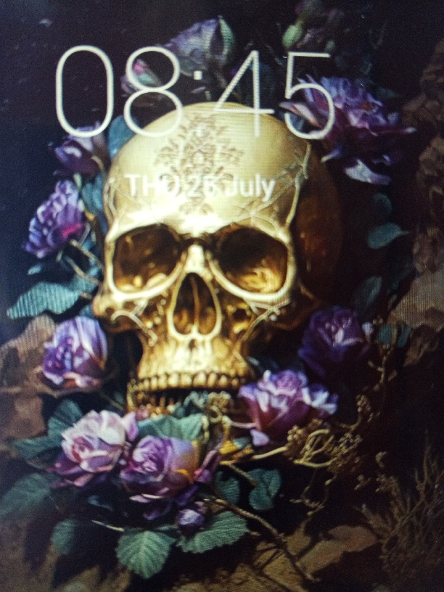 A digital image of a lock screen displays a golden skull surrounded by purple roses against a dark, textured background. The time 08:45 and the date "THU 26 July" are superimposed at the top. The location in the city of Tinaquillo, Venezuela is not discernible in the image. There are no people visible.
