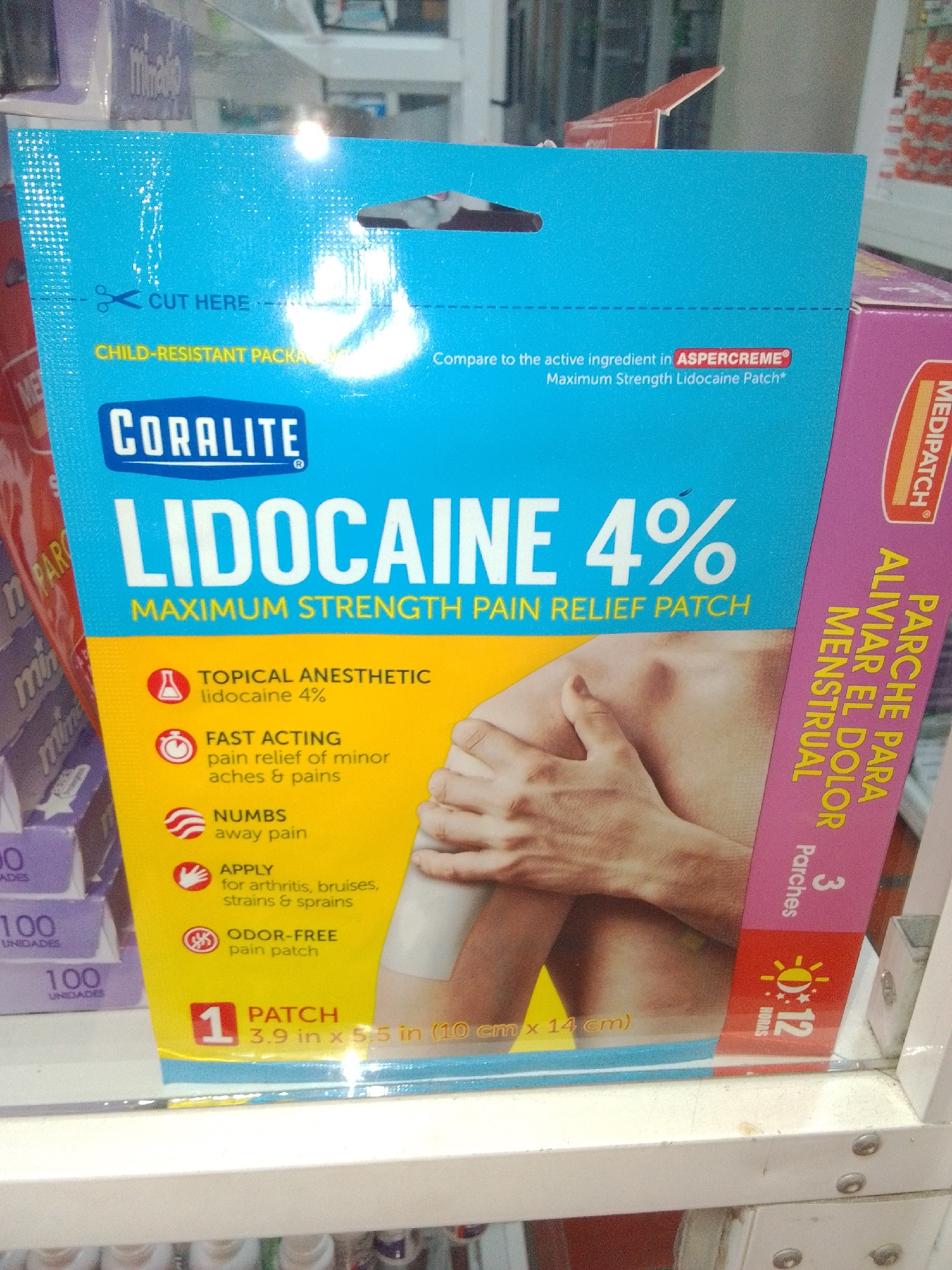 The image shows a product box for "CORALITE LIDOCAINE 4% MAXIMUM STRENGTH PAIN RELIEF PATCH". The box is predominantly blue and yellow, with an image of a person's arm and shoulder with a patch applied. Text on the box indicates it is a topical anesthetic, fast-acting, numbs pain, is for arthritis, bruises, strains & sprains, and is odor-free. It also states it contains 1 patch, measuring 3.9 in x 5.5 in. A pink side panel of another product, "MEDIPATCH PARCHE PARA ALIVIAR EL DOLOR MENSTRUAL" (Medipatch Patch to relieve menstrual pain), is visible on the right. The product is displayed on a shelf, likely in a retail environment such as a pharmacy or store. The context of Juan Griego, Venezuela is not evident from the visual information in the image.