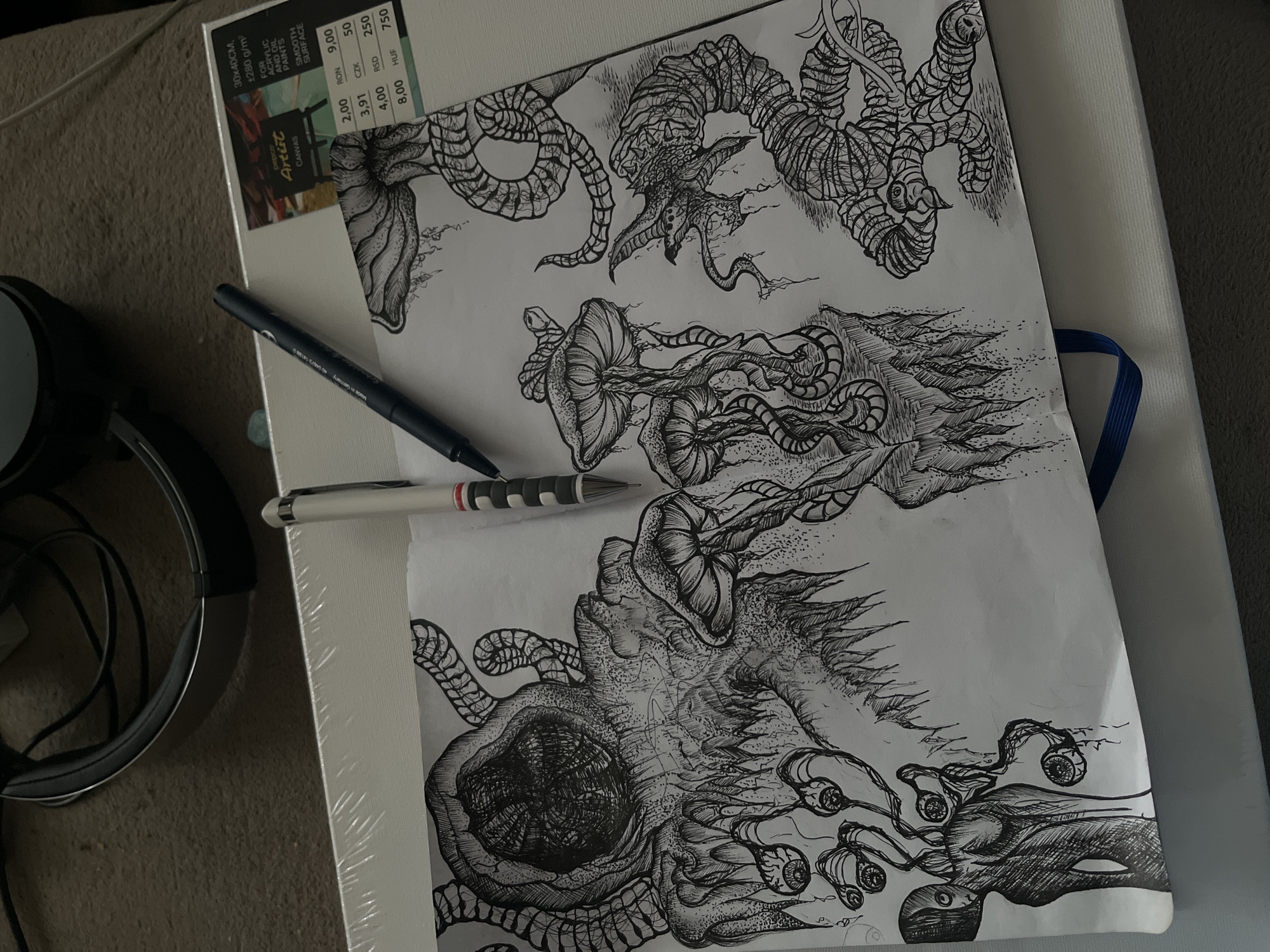 An overhead shot captures a detailed black and white ink drawing resting on a white stretched canvas, surrounded by various items on a textured brown surface. The drawing itself is highly intricate, depicting several fantastical, organic-looking forms that resemble deep-sea organisms or surreal biological structures. These forms are rendered with extensive cross-hatching and stippling, creating rich textures, shading, and a sense of depth, featuring tentacles, bulbous shapes, and eye-like elements.
Two pens are visible on the paper and canvas: a dark blue pen with a silver clip, which has "Made in Germany" printed on its barrel, and a white pen with black and red striped accents. A portion of the white stretched canvas is visible beneath the drawing, displaying a label that reads "30x40CM, +280 g/m²", identifying it as "pepco Artist Canvas" suitable "FOR ACRYLIC AND OIL PAINTS SMOOTH SURFACE". The label also lists prices in several currencies: "RON 2,00", "CZK 3,91", "RSD 4,00", and "HUF 8,00".
To the left of the artistic materials, a pair of black over-ear headphones with an attached cable rests on the brown, possibly carpeted, surface. The scene suggests an indoor setting and an ongoing or recently completed artistic endeavor. While the provided context indicates the location is Sofia, Bulgaria, there are no specific visual cues within the image itself to confirm this.