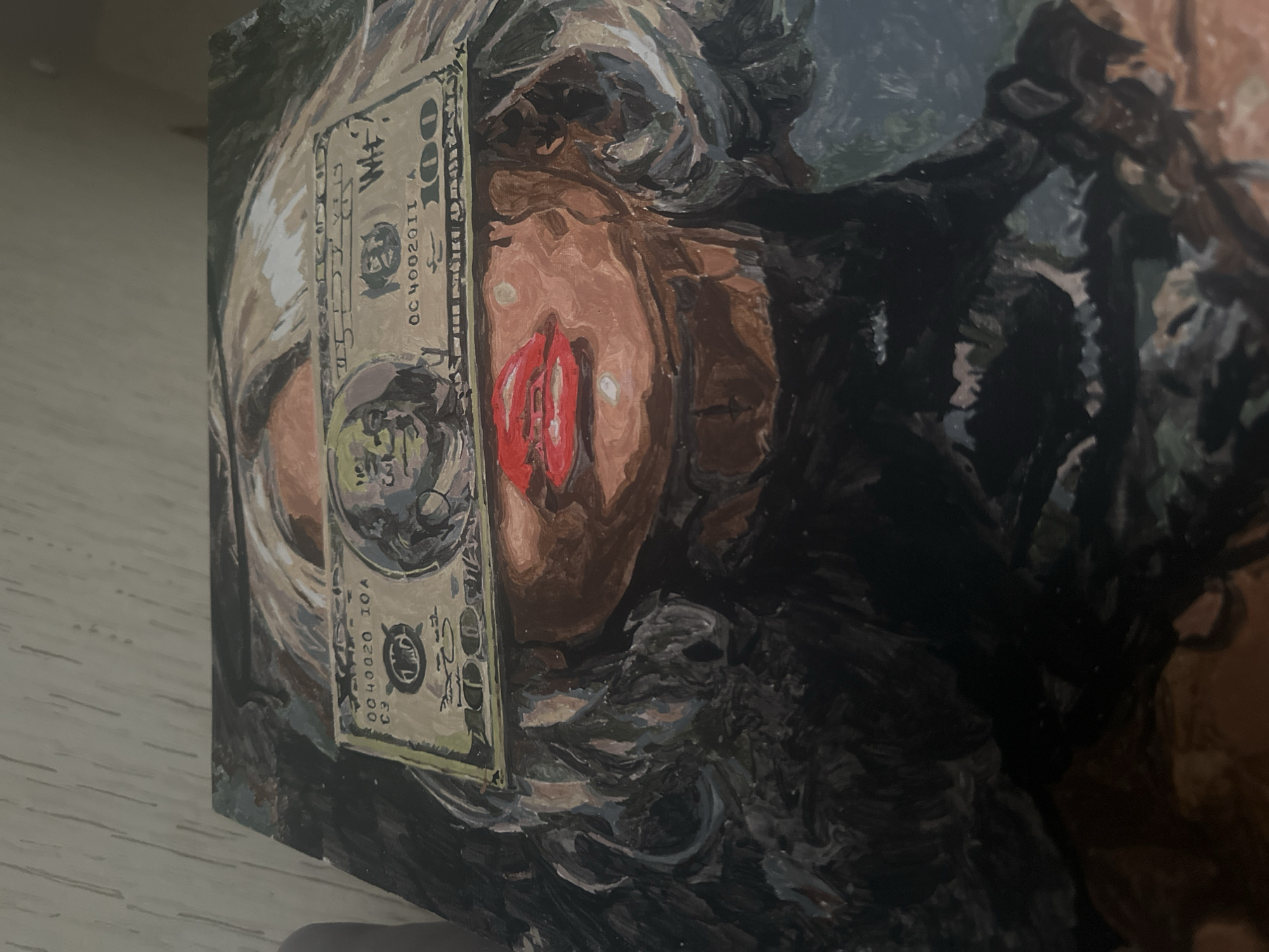 The image shows an oil painting depicting a partially obscured face with a US $100 bill overlapping the eye and cheek. The face is painted with brown skin, with red lips and dark hair. The bill is depicted vertically, with a portrait of Benjamin Franklin. The painting is positioned on a light-colored, smooth surface. The exact location in the city of Высокий, Russia, is not ascertainable from the image.