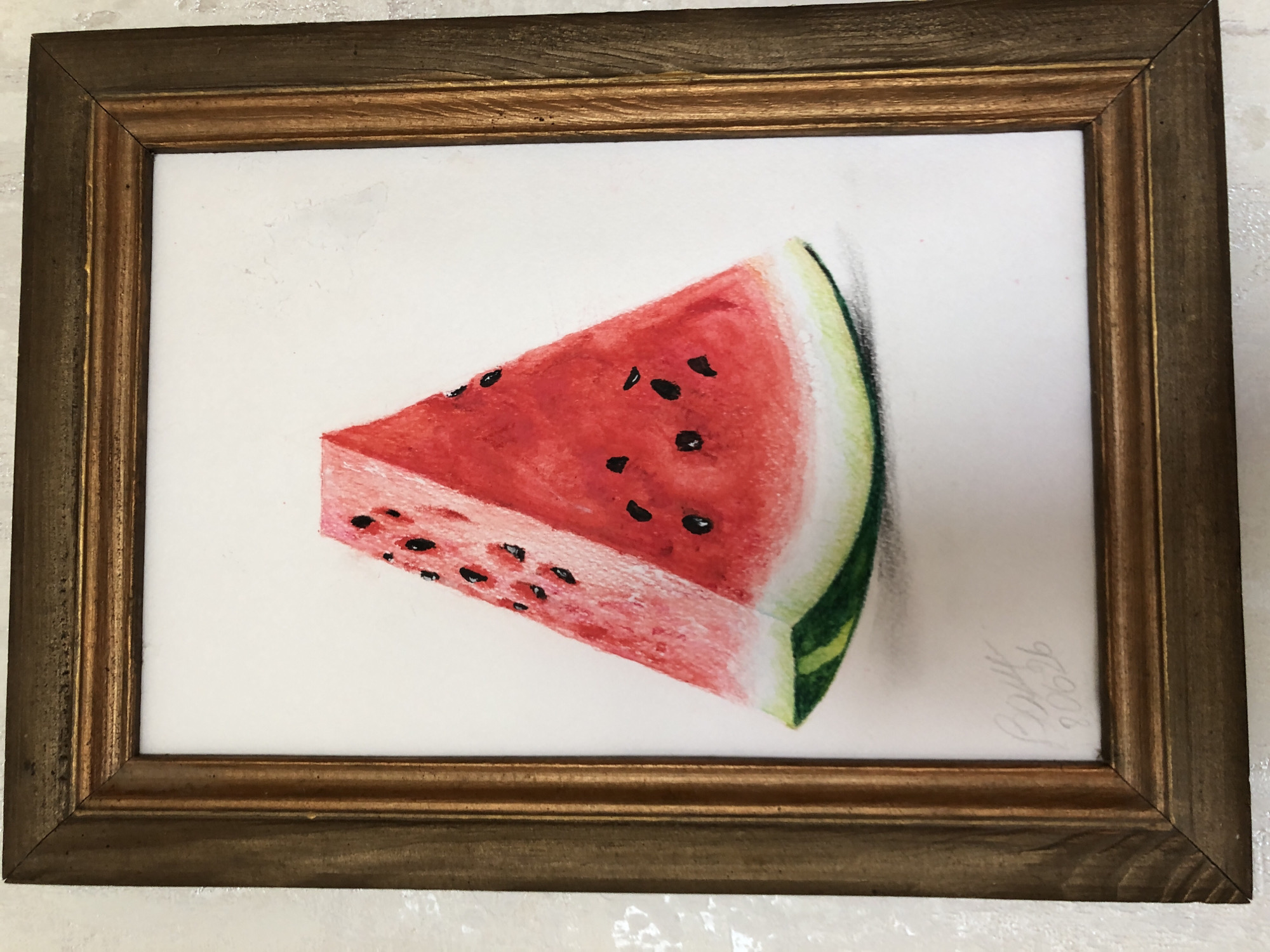 A framed watercolor painting of a slice of watermelon is displayed against a textured white wall. The watermelon slice is depicted as a wedge with vibrant red flesh, black seeds, and a green rind. The painting is signed in the lower left corner with the text "Rory 2026" in a light grey, handwritten script. The frame is made of wood with a distressed antique gold finish.