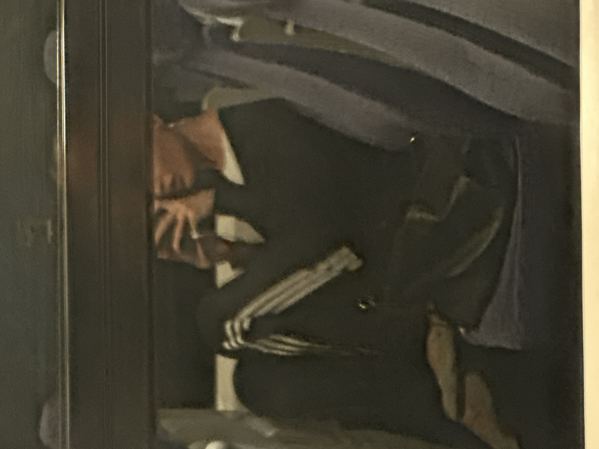 The image is a photograph of a framed painting. The painting depicts a figure in dark clothing, possibly kneeling or crouching. A visible skeletal hand and foot are present. The background consists of a grey or blue shaded area, potentially representing fabric or a cloud. The painting is framed in a dark-colored frame. It is not possible to ascertain the location or any other information based on the picture.