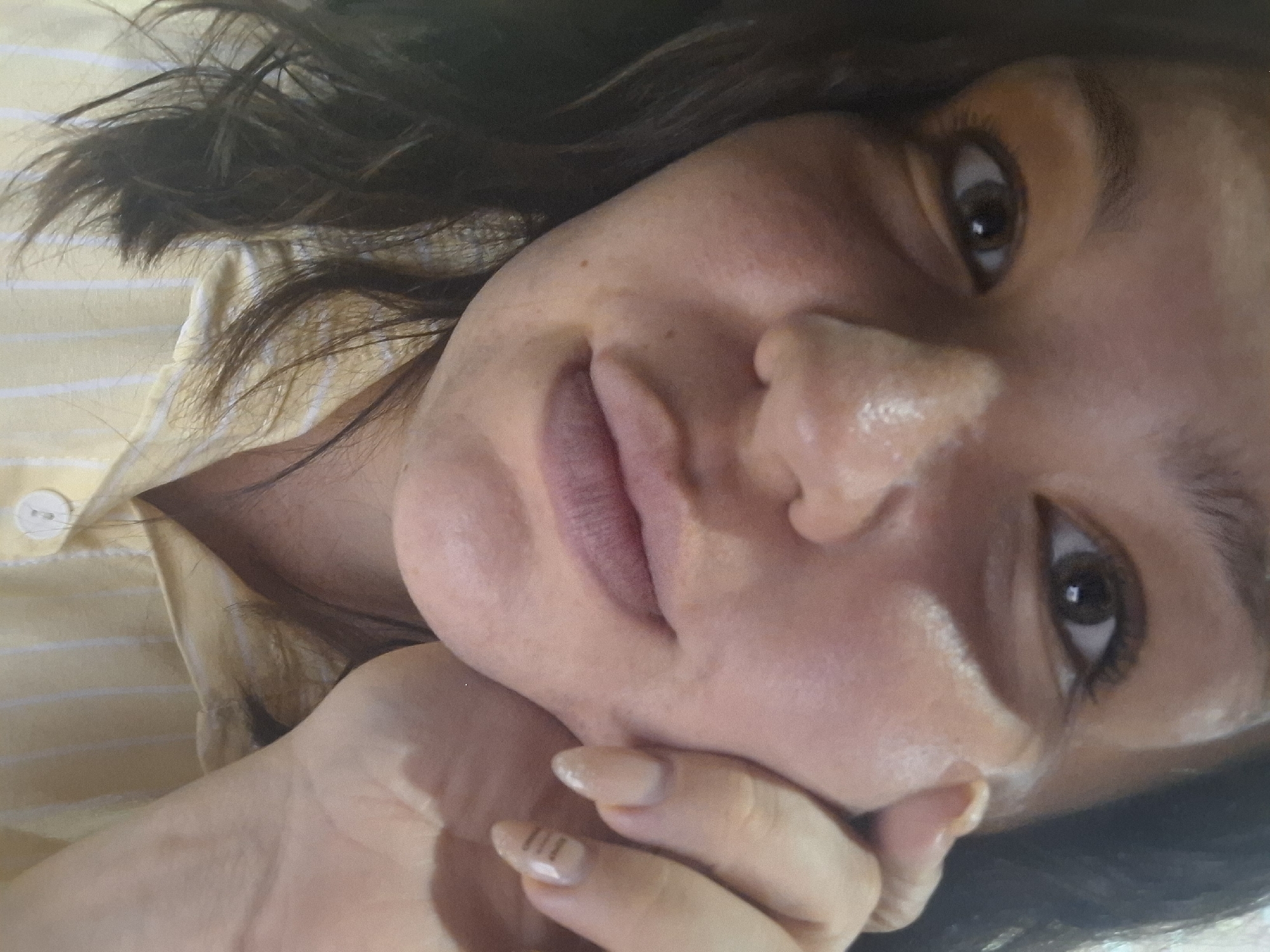 A close-up, angled selfie captures a person with brown eyes and short, dark brown hair. The person is wearing a light yellow shirt with white stripes and a white button visible on the collar. The person's left hand is raised to their face, with fingers touching their lips. The location is unknown, and there is no evidence to suggest this photo was taken in Марковский, Russia.