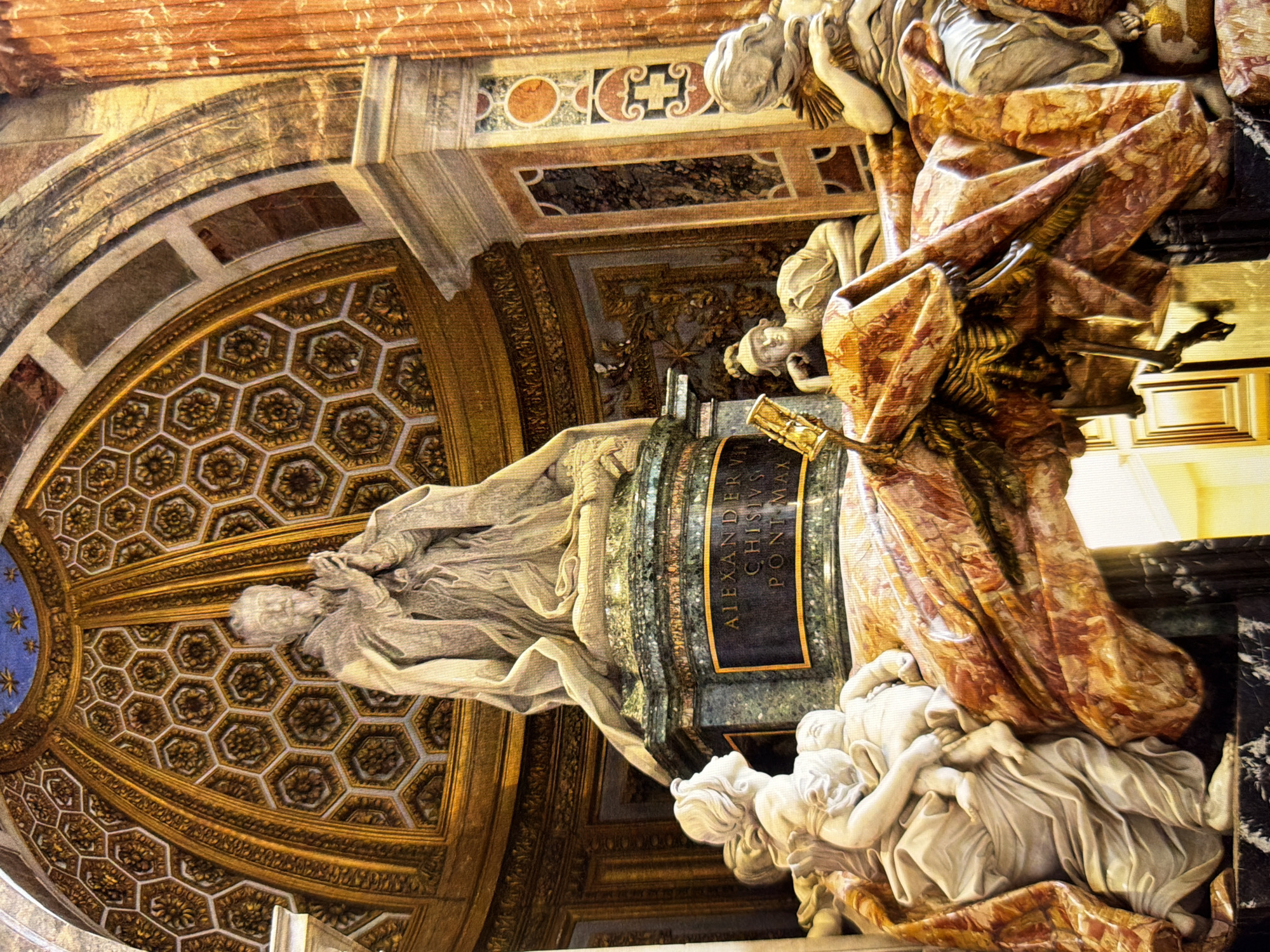 The image shows a detailed view of Bernini's *Tomb of Pope Alexander VII* located in St. Peter's Basilica in Vatican City. The sculpture depicts Pope Alexander VII in prayer, robed and seated on a pedestal inscribed with "ALEXANDER VII CHISIVS PONT MAX". Around the pedestal, allegorical figures represent virtues. A woman holding an infant is on the left, a skeleton with an hourglass is in the center, and a reclining figure is on the right. The background features a richly decorated dome and architectural elements made of marble and gold. The scene is indoors, within a grand ecclesiastical setting. There is no indication of the location being Kyiv, Ukraine.