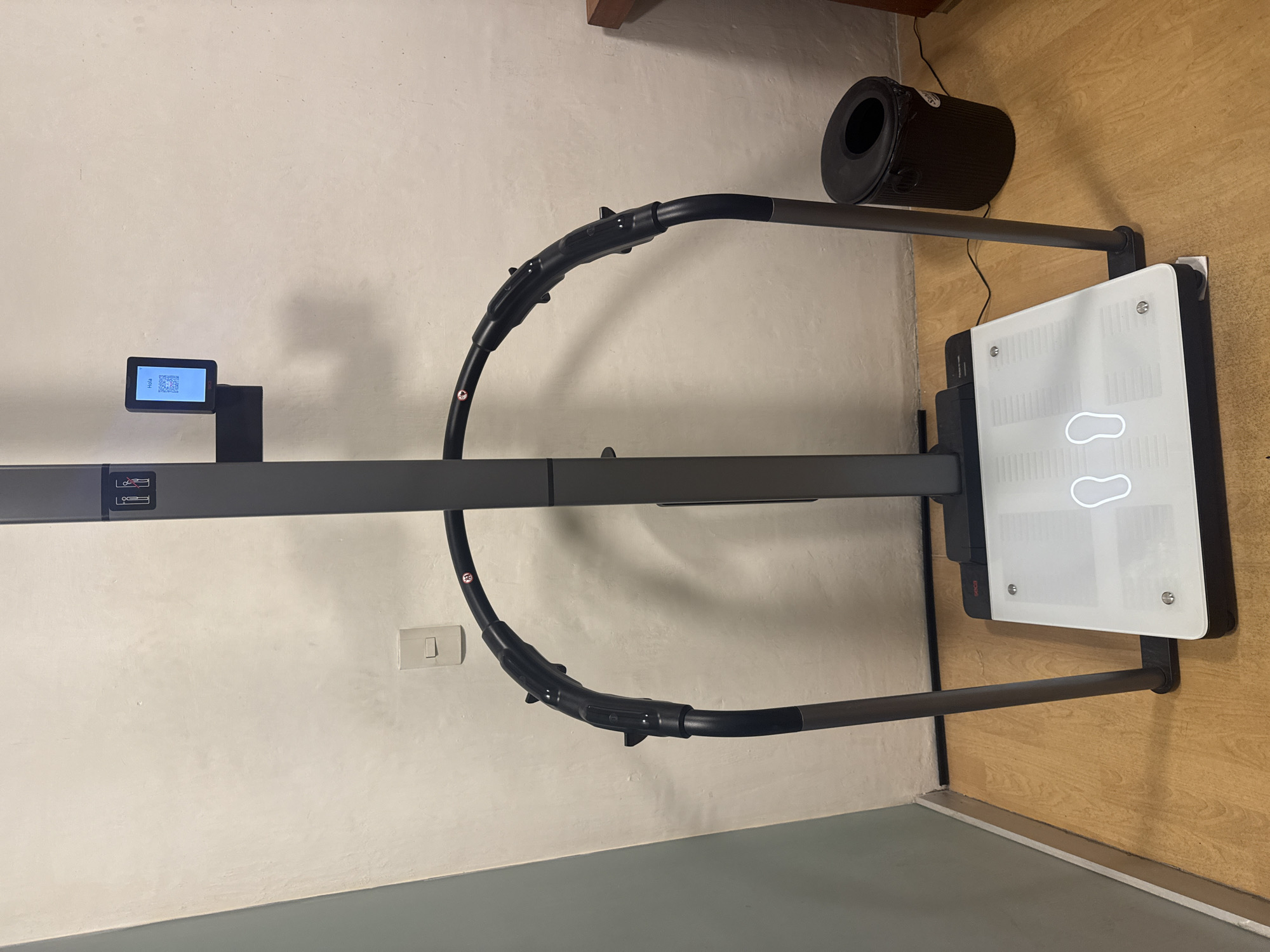 The image depicts a white and gray body composition analyzer, likely for medical or fitness purposes, placed against a wall in a room. The analyzer features a foot placement guide on a white platform, supported by a gray frame. A small monitor on the left displays information, possibly a QR code. An air purifier or filter is placed next to the analyzer on a wooden floor. The environment appears to be an indoor space, possibly a clinic, gym, or laboratory. The location is Puebla, Mexico.