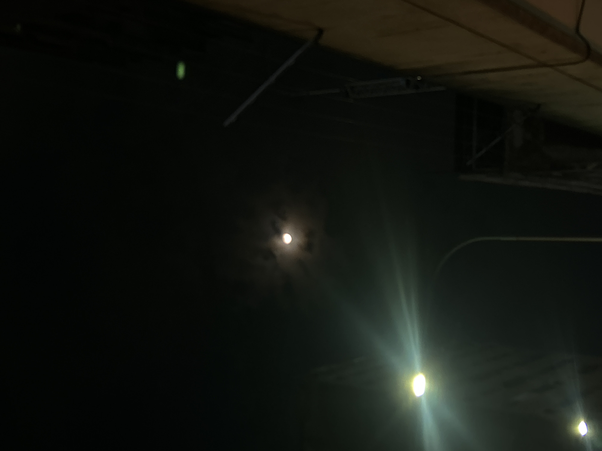 The image, taken at night, features the moon visible in the sky. The illumination from streetlights is evident in the lower right corner. Some sort of infrastructure (roofing) is visible at the top. The photo may be in Caracas, Venezuela, but this cannot be confirmed from the scene alone.