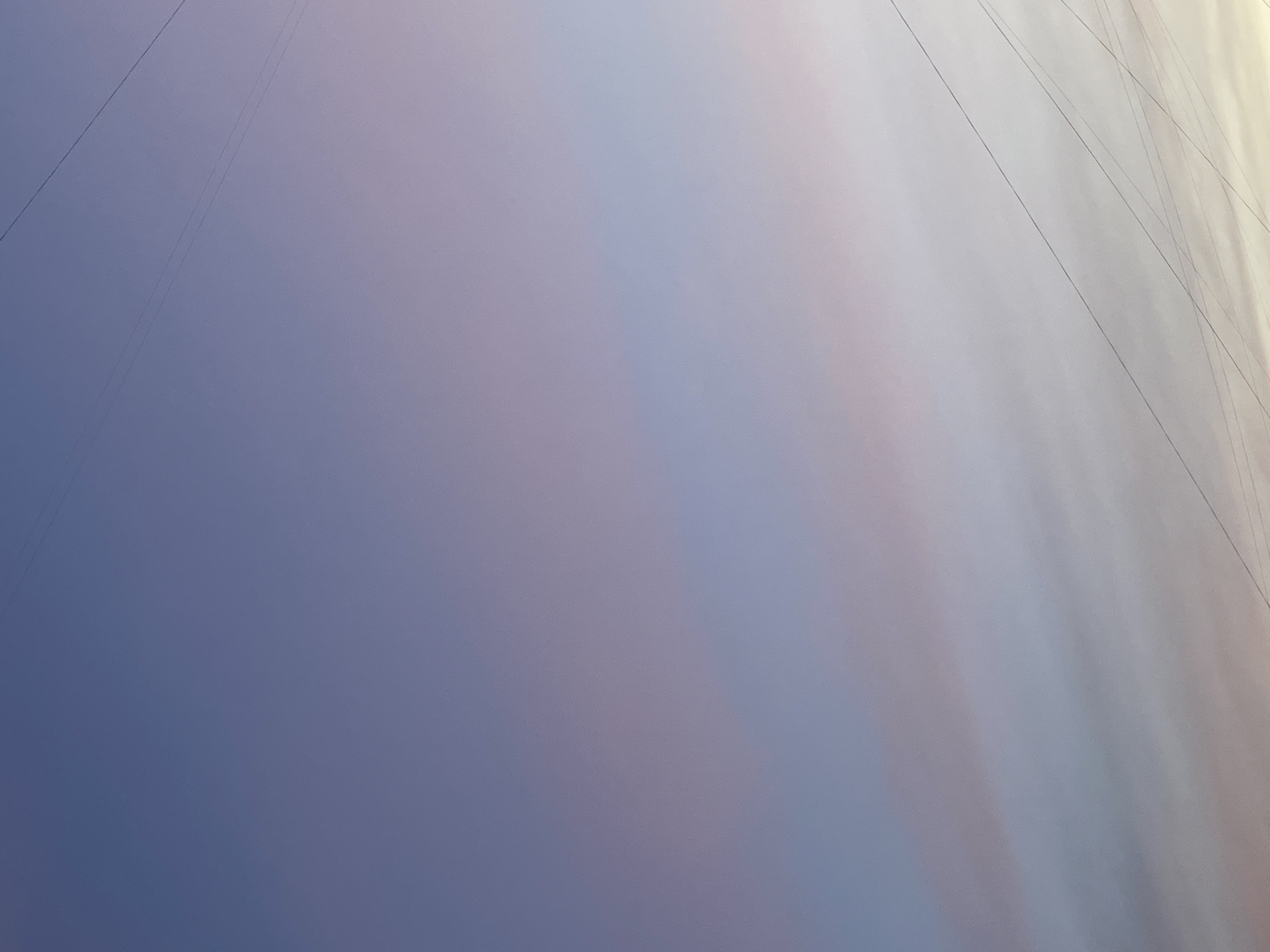 A sky scene captured from the city of Krasnogorsk, Russia, during either dawn or dusk. The sky displays a gradient of soft colors, transitioning from a pale purple at the top to lighter shades of pink and white towards the bottom. Thin, dark utility wires are visible crisscrossing the sky in several places. No people, animals, or buildings are present in the frame.