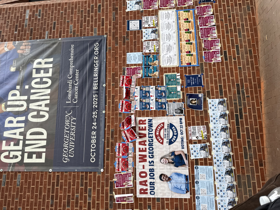 The image displays a densely covered reddish-brown brick wall on the campus of Georgetown University in Washington, D.C., United States, functioning as a public bulletin board. A large, dark blue banner at the top advertises the "GEAR UP. END CANCER." event for the Georgetown University Lombardi Comprehensive Cancer Center, scheduled for October 24-25, 2025, with a partial image of a cyclist. Below this banner, the wall is extensively covered with numerous paper posters and flyers of varying sizes, adhered haphazardly.
Prominently featured in the center is a large campaign poster for "RAO-WEAVER OUR JOB IS GEORGETOWN," displaying smiling photographs of a man and a woman, with "RAO-WEAVER OUR JOB IS GEORGETOWN FOR GUSA" and "VOTING: OCT 22 8PM" indicated. Surrounding this central poster are dozens of smaller flyers. Many repeat messages such as "MY BODY, MY CHOICE! Vote Ann Johnson" (pink/purple), "A BETTER WORLD... A BETTER GEORGETOWN" (red with QR codes), and various "Match-up" posters with candidate names and QR codes, likely related to student elections. Other visible posters announce events like "Rally for Gaza," "Gospel of John Bible Study," and provide information for the "Financial Accessibility and Equity Committee," or promote organizations like "The Philodemic Society." The ground at the bottom of the wall is paved, and a partial view of a dark object and a white bottle is visible in the lower left foreground.