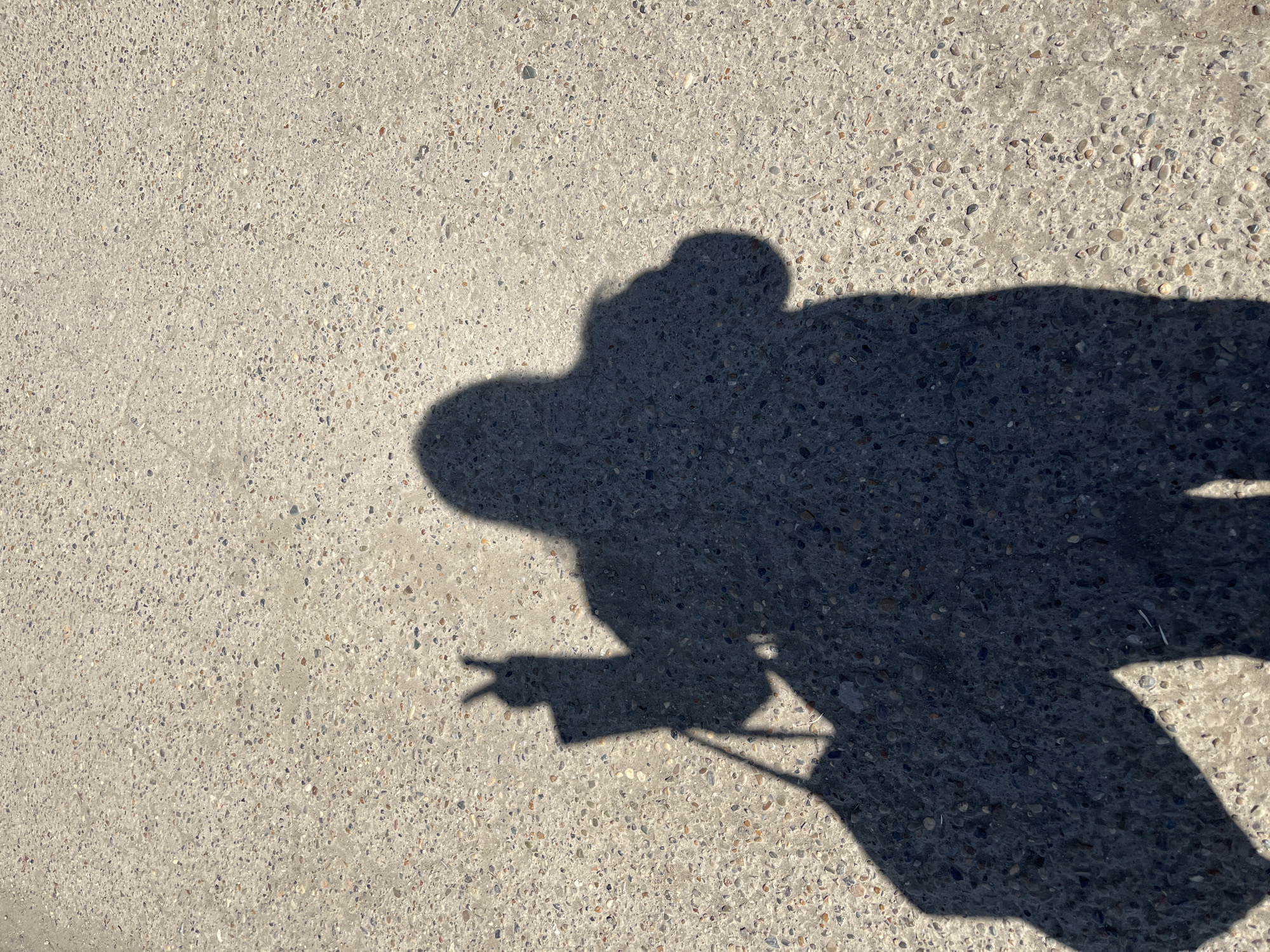The image shows the shadow of a person on a concrete surface. The shadow is dark and distinct, suggesting a bright light source. The person is making a peace sign with their hand. There is no explicit information linking the location to Izhevsk, Russia.